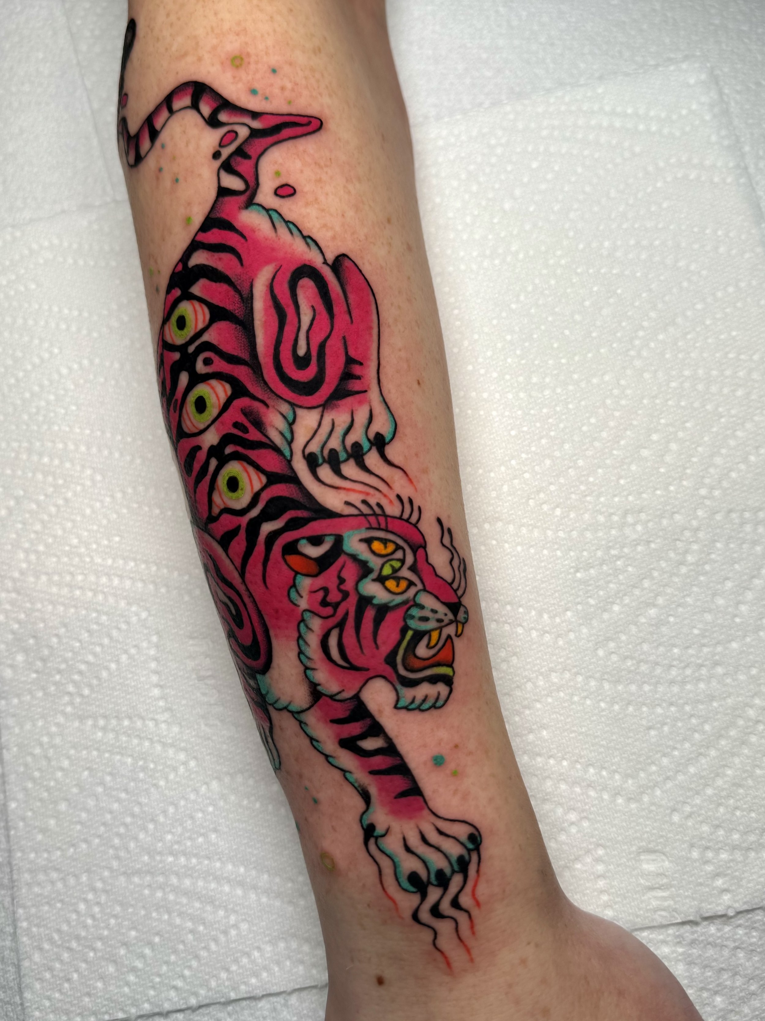 Tattoo of a pink and black tiger with a stylized, surreal design on a person's arm.