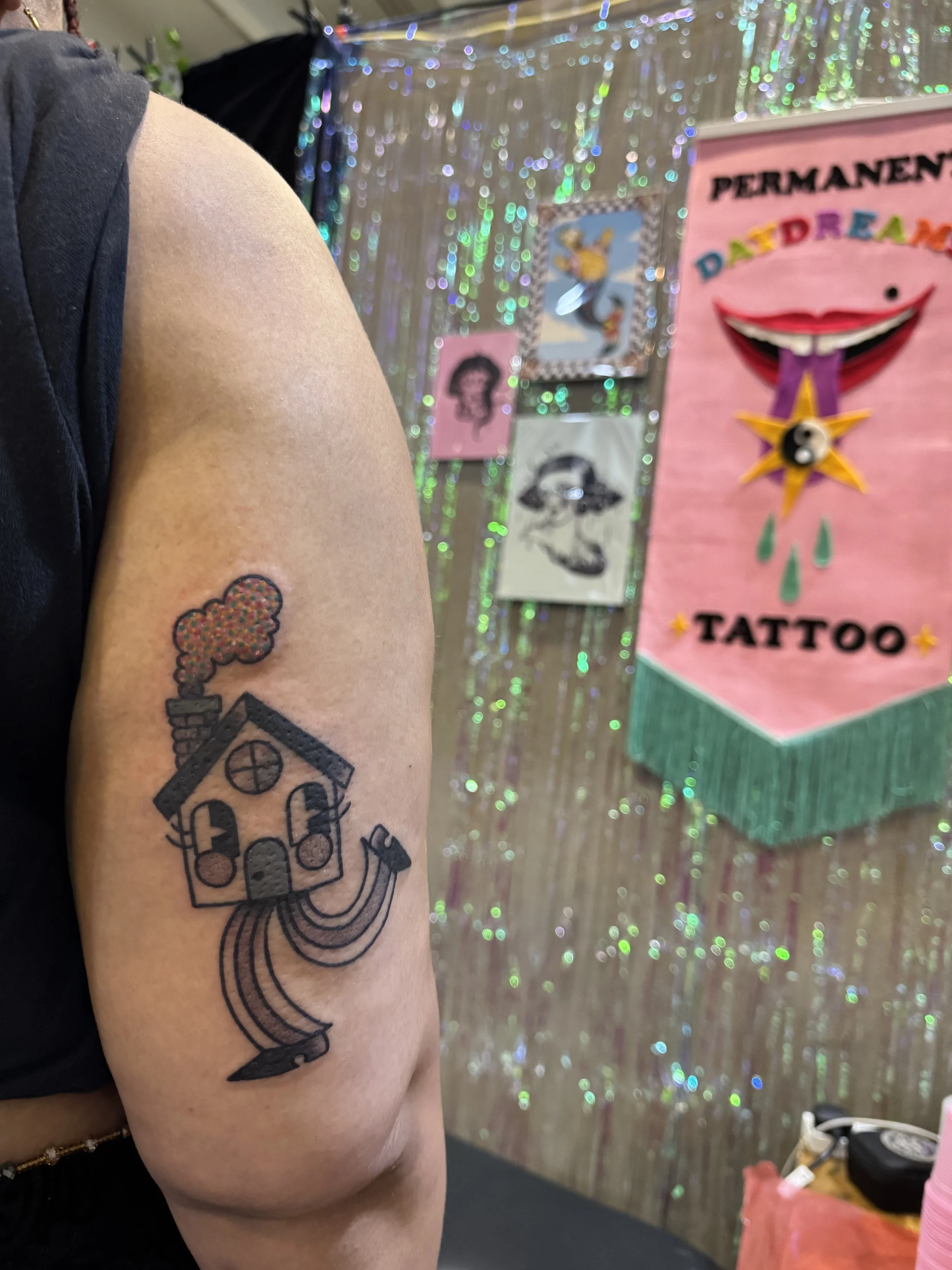 Tattoo of a house with a chimney emitting colorful rainbow smoke, wearing trousers.