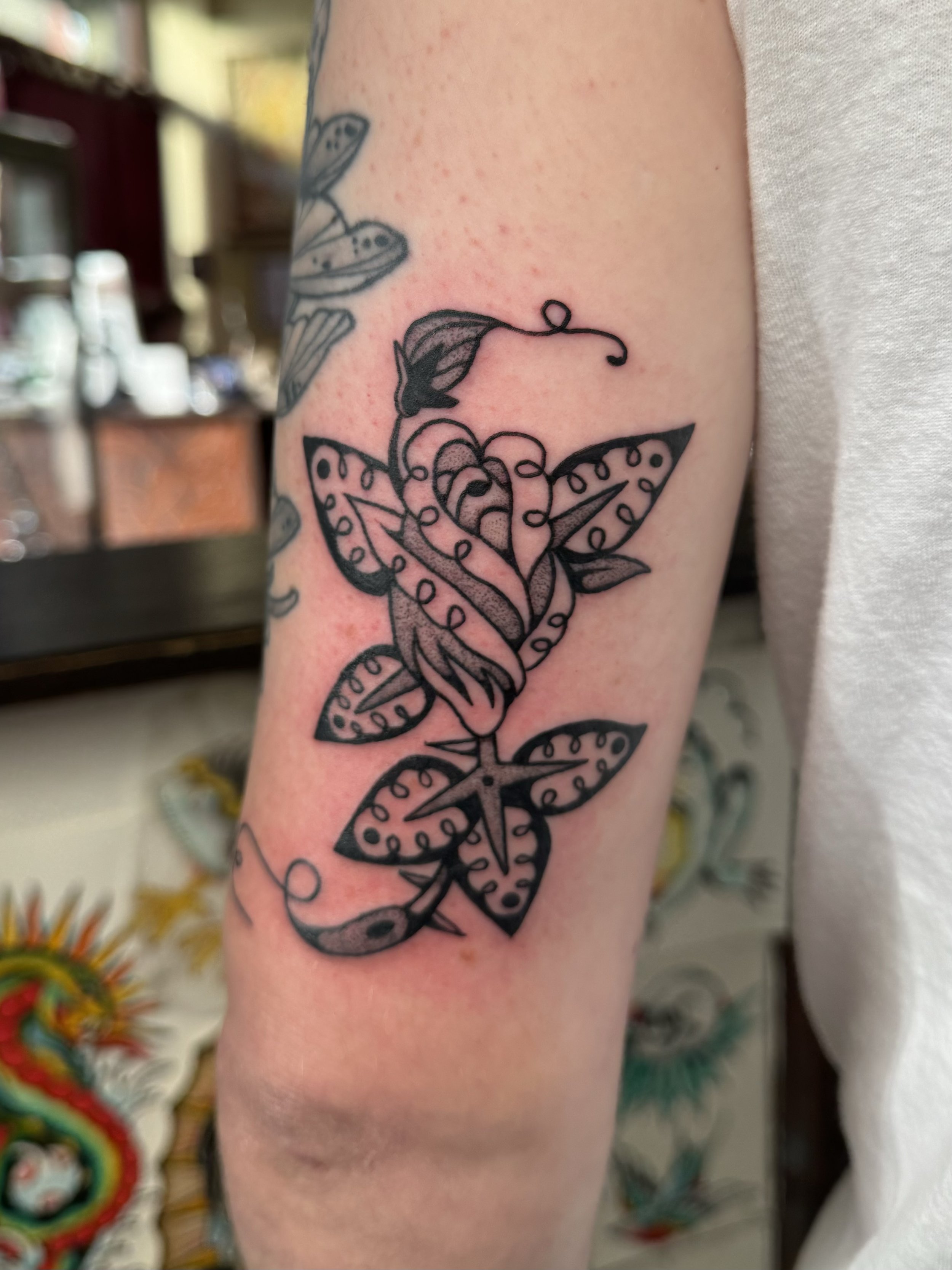 Black ink tattoo of a rose with intricate designs and leafy details on a person's upper arm.