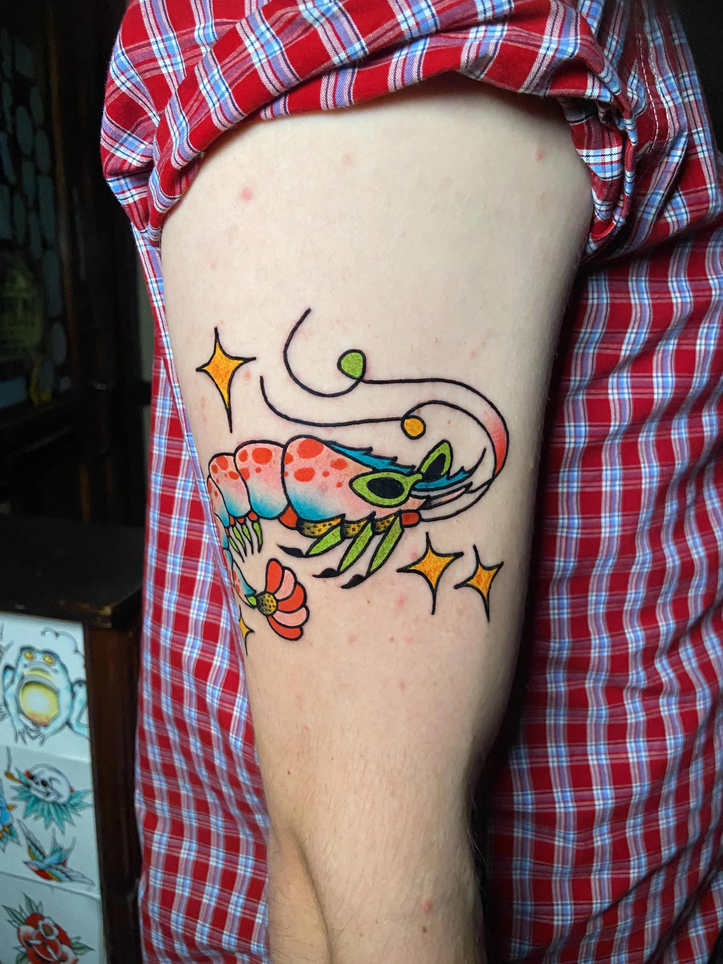 Colorful tattoo of a shrimp with sunglasses, surrounded by stars and swirling lines on a person's arm.