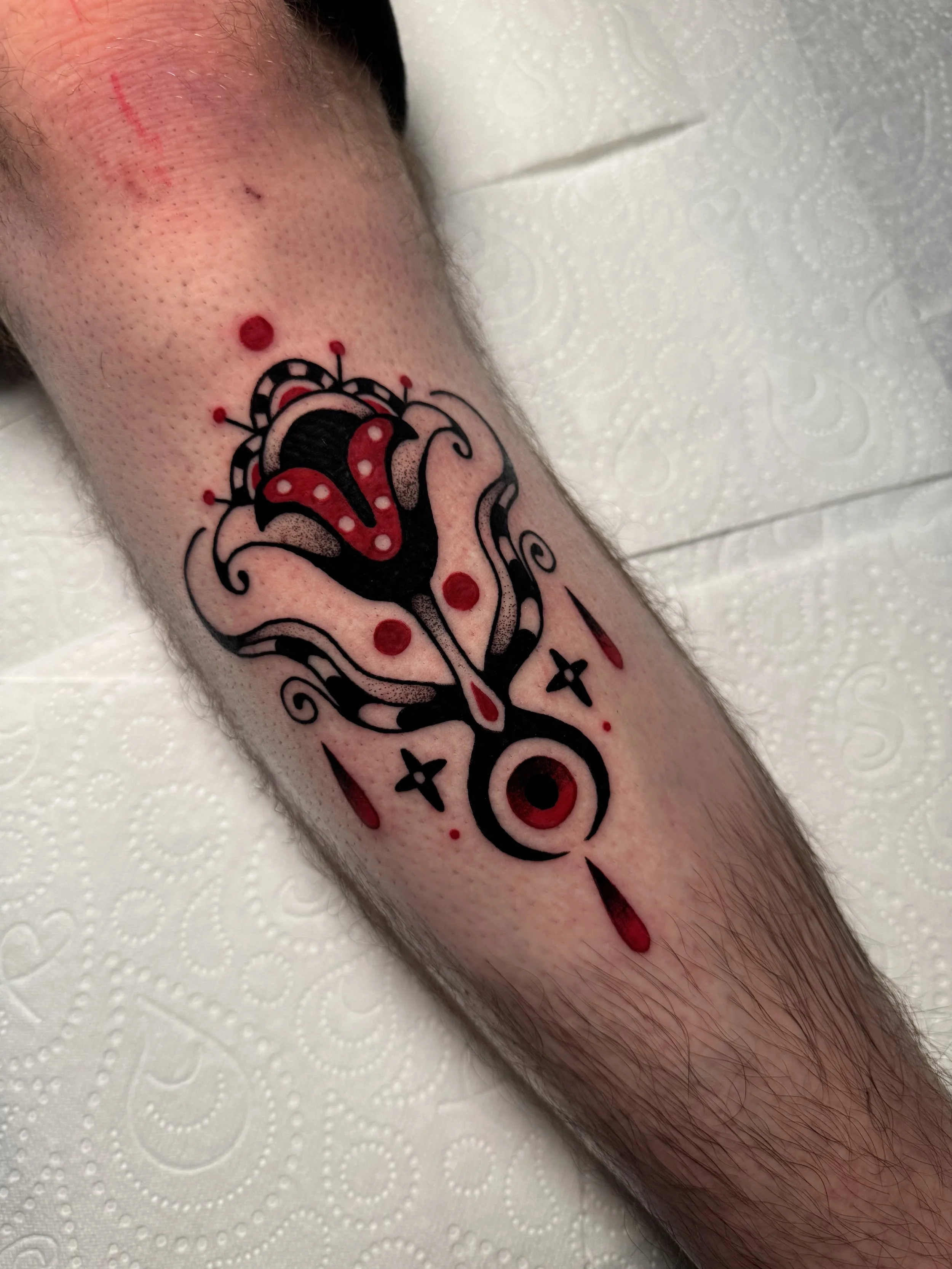 Tattoo of a stylized, abstract flower with red and black accents on a person's shin. Tribal tattoo vibes.