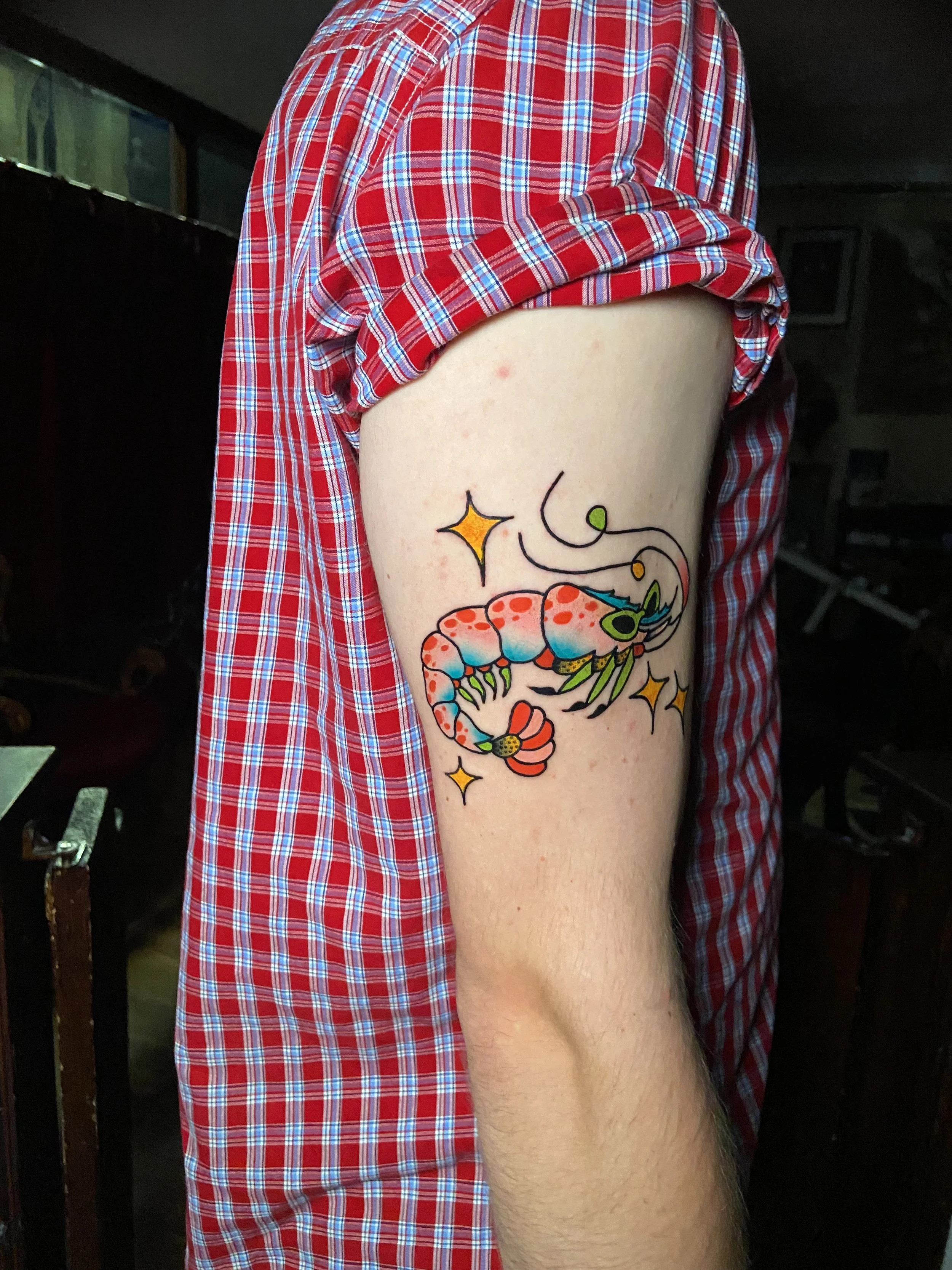 Tattoo of a colorful shrimp surrounded by sparkling stars on a person's upper arm.