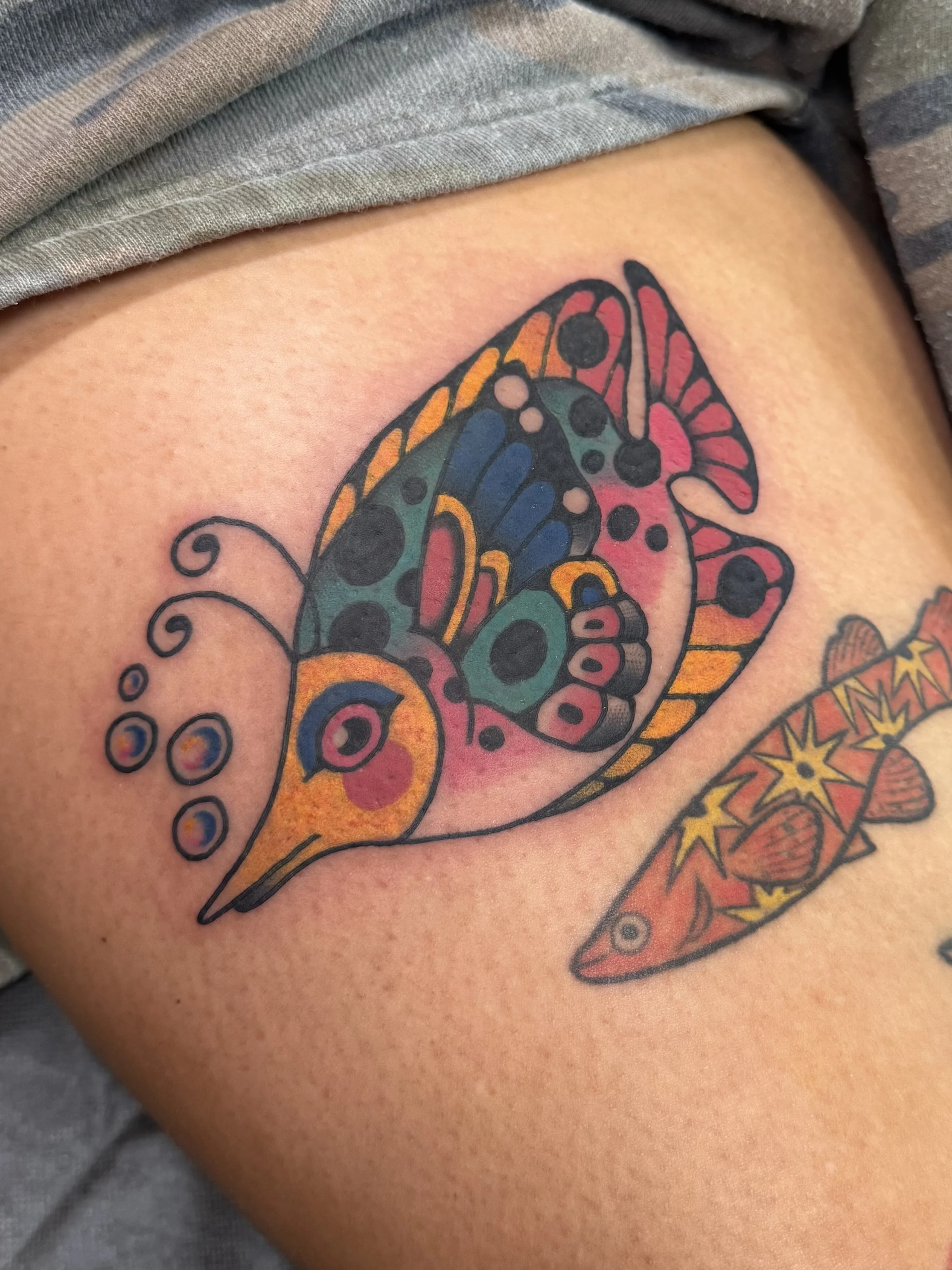 Colorful butterfly fish tattoo with geometric patterns and dots on skin.