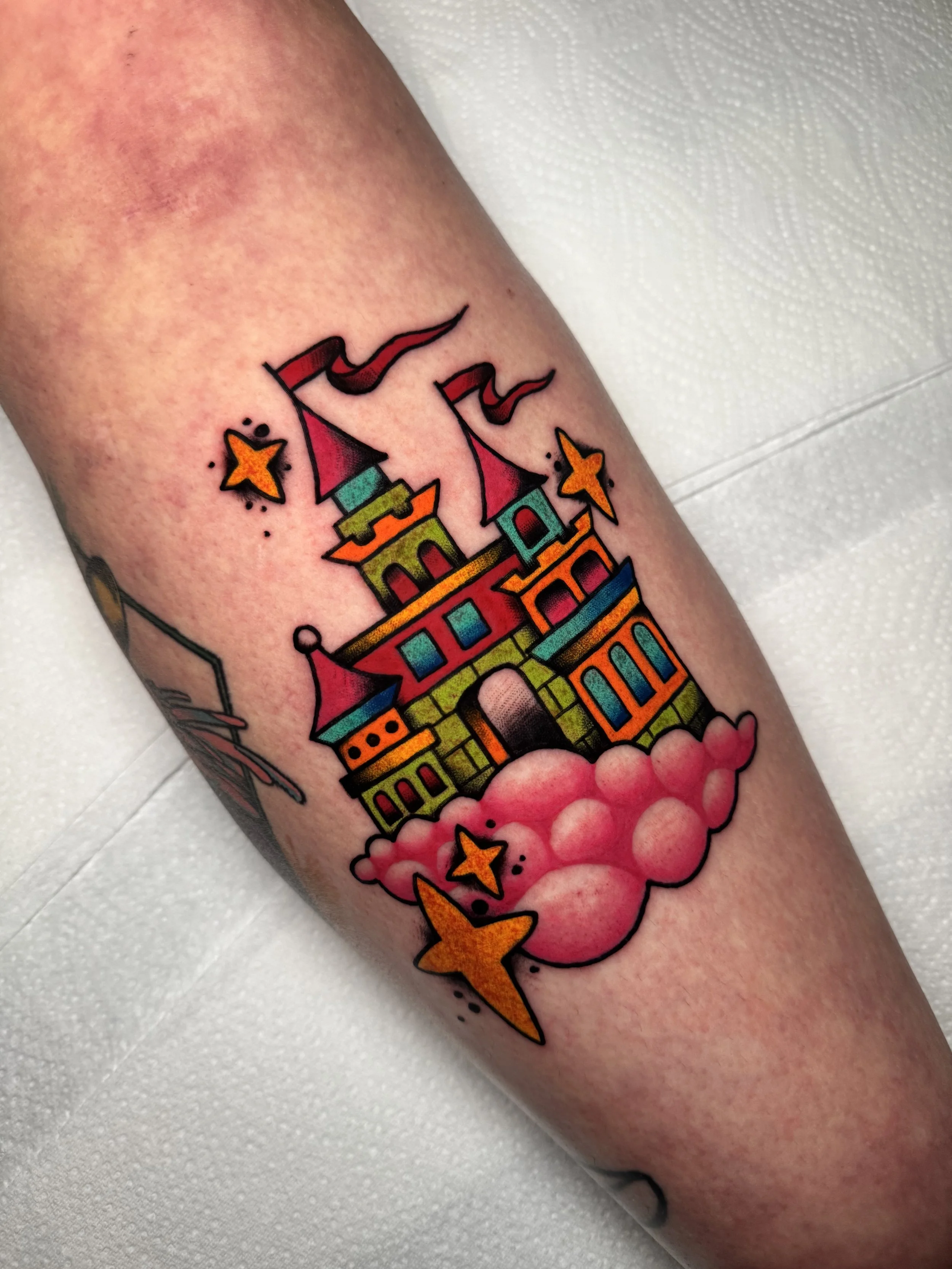 Colorful tattoo of a castle with pink clouds and stars.