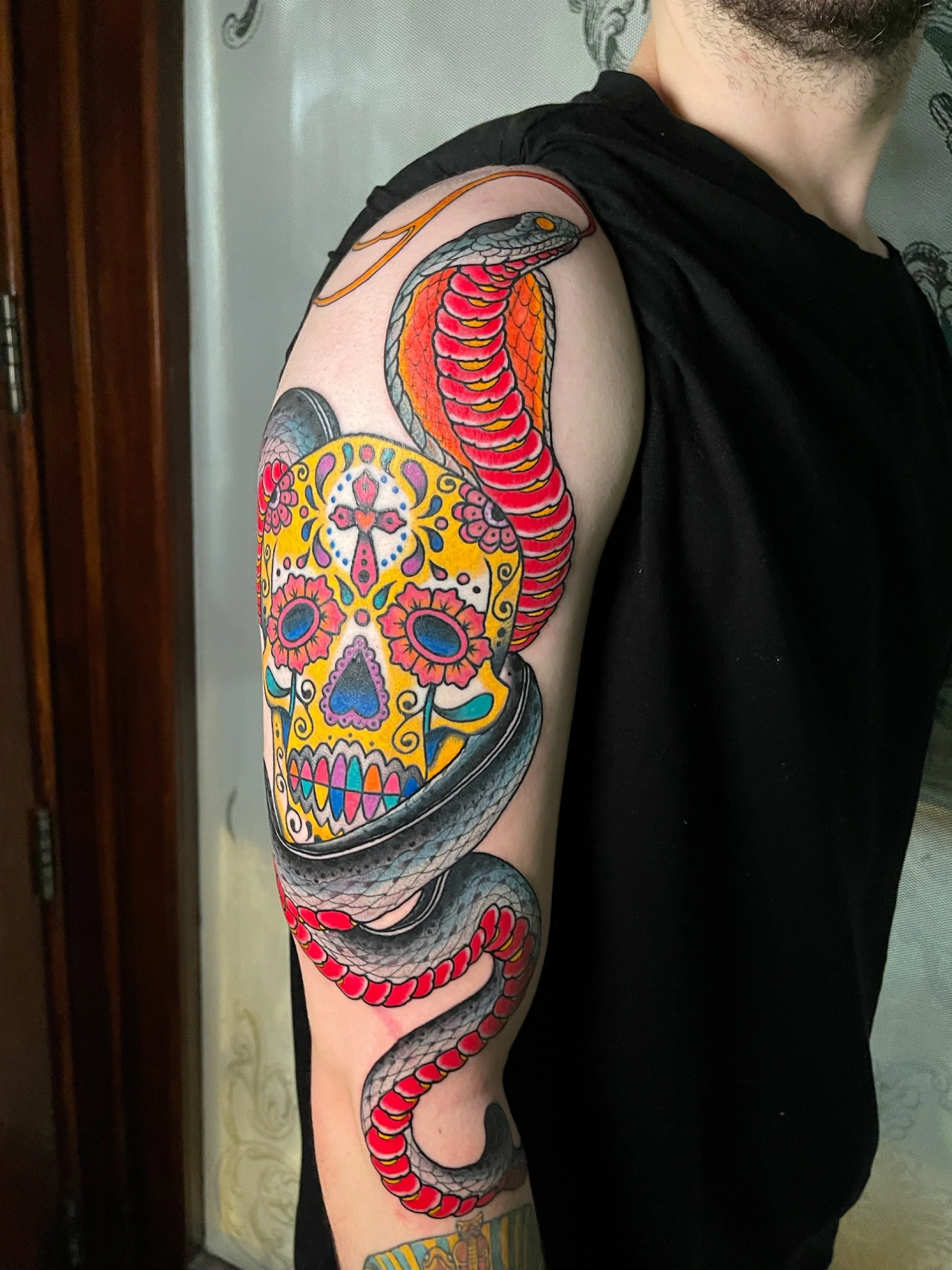 Colorful tattoo of a sugar skull and a snake on a person's upper arm.