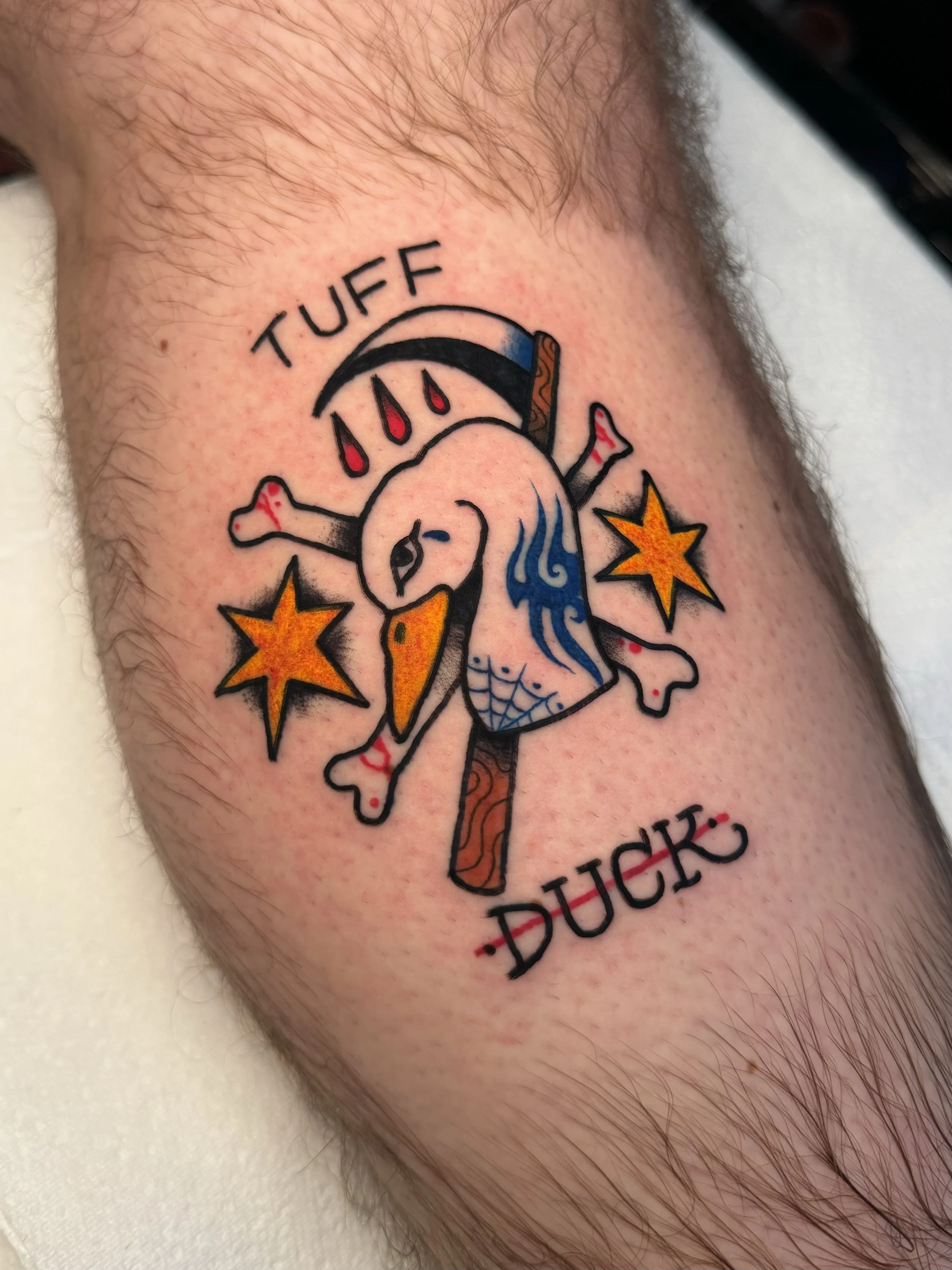 Tattoo of a cartoon duck with a scythe, surrounded by stars, bones, and blood drops, with the words 'TUFF DUCK' above and below.