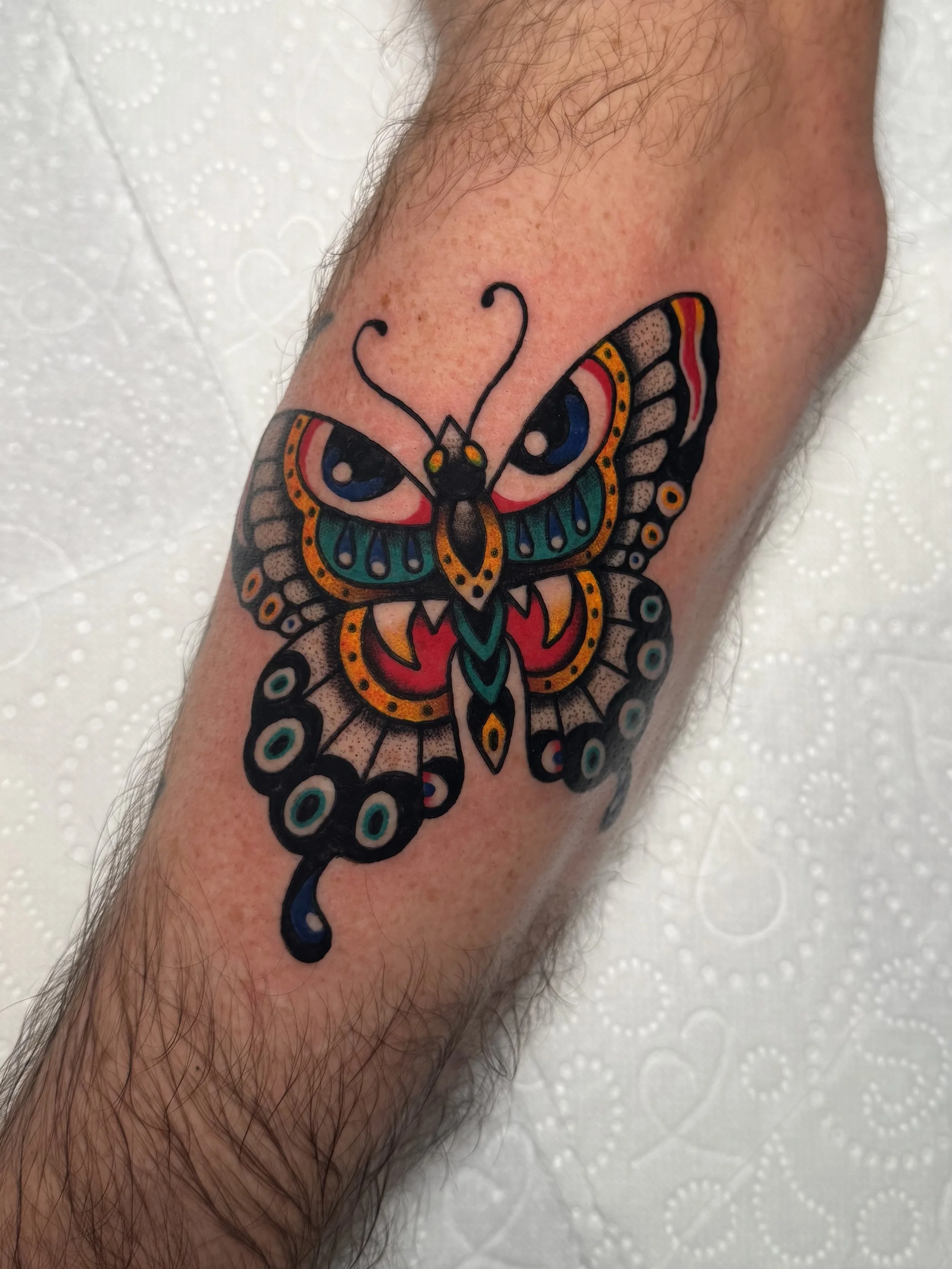 Colorful butterfly tattoo with bold black outlines on person's forearm.