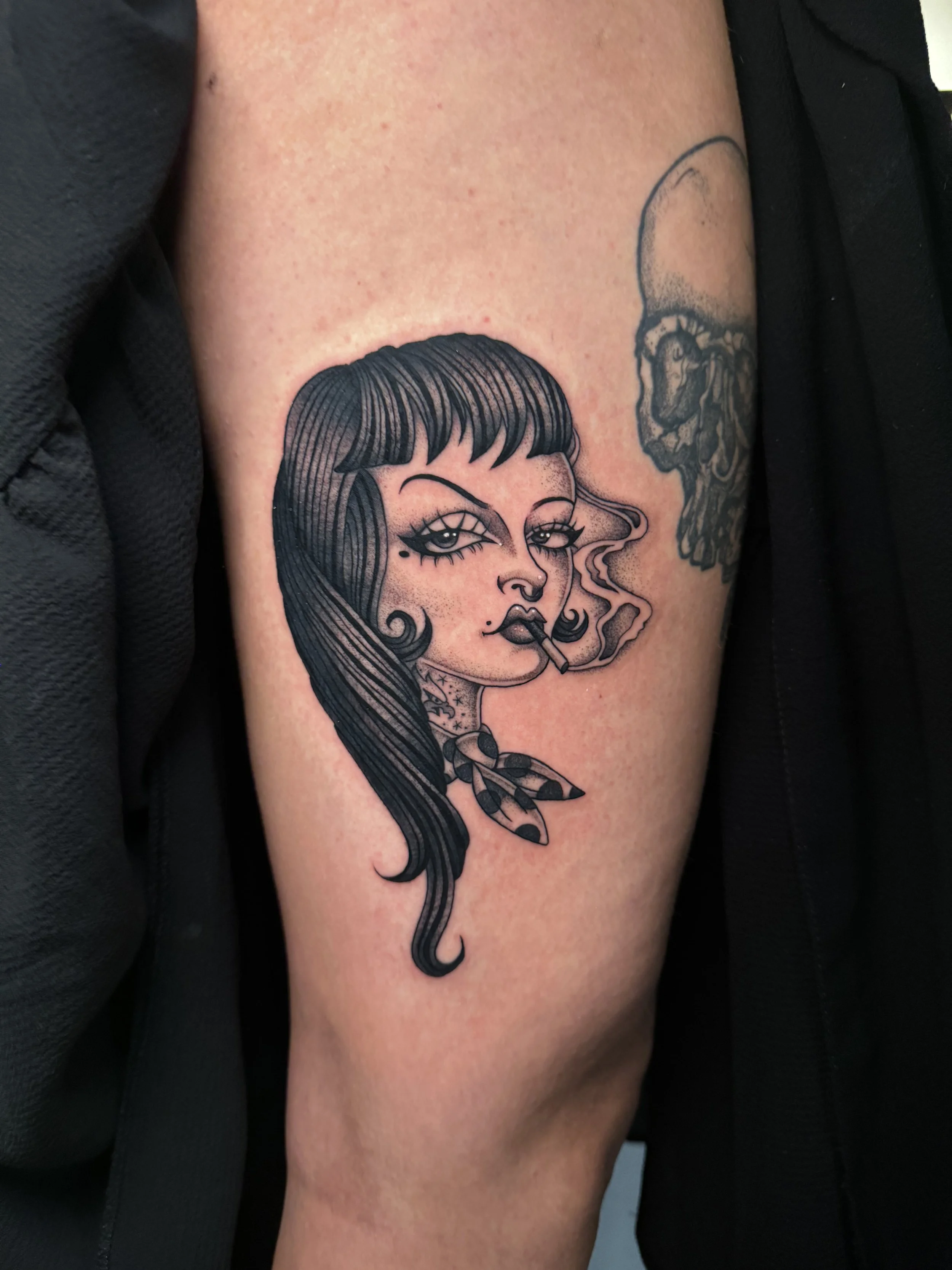 Tattoo of a woman with dark hair, bangs, and makeup, smoking a cigarette, with a scarf around her neck.