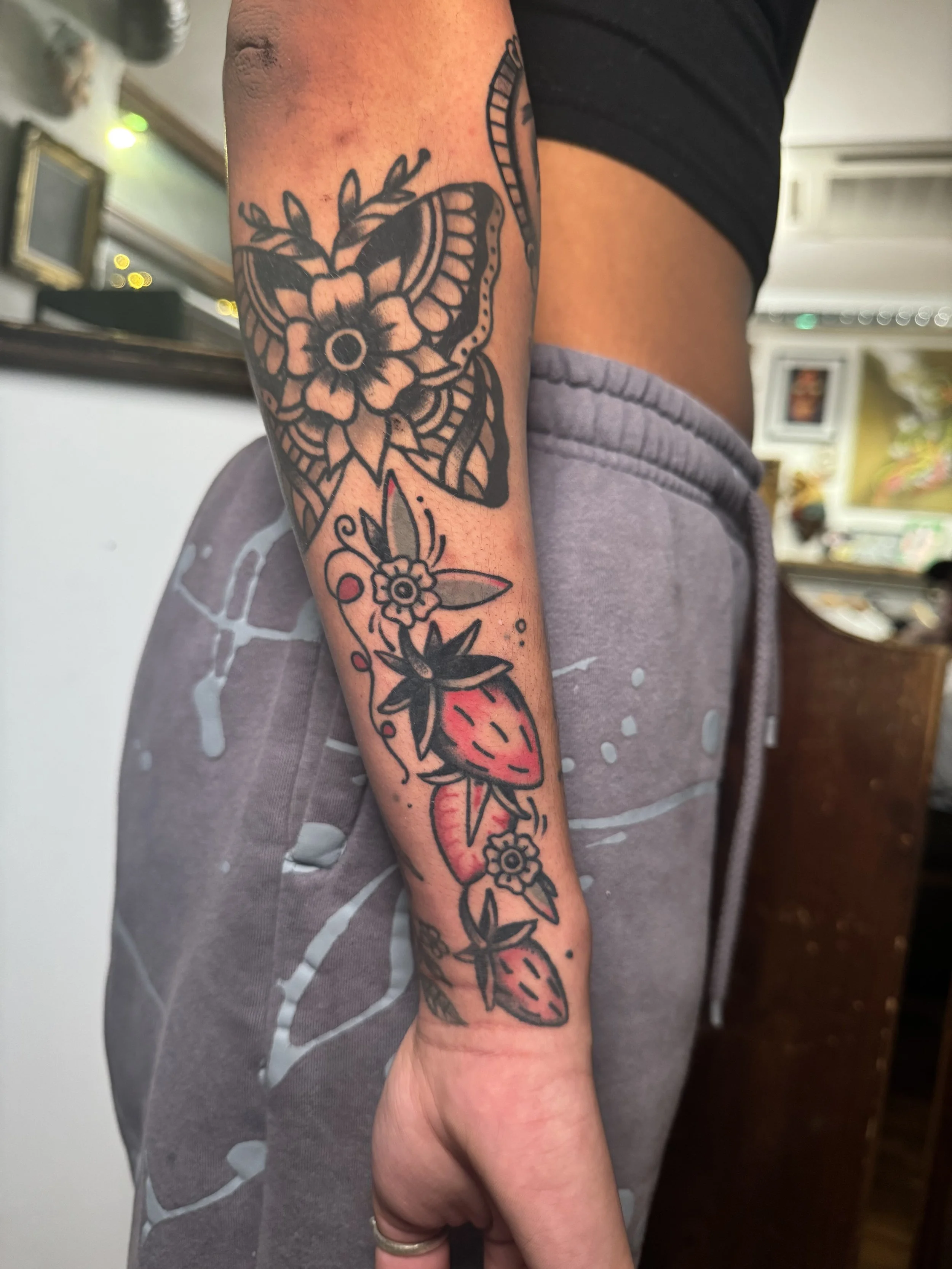 Tattoo of strawberries and flowers on a person's forearm.