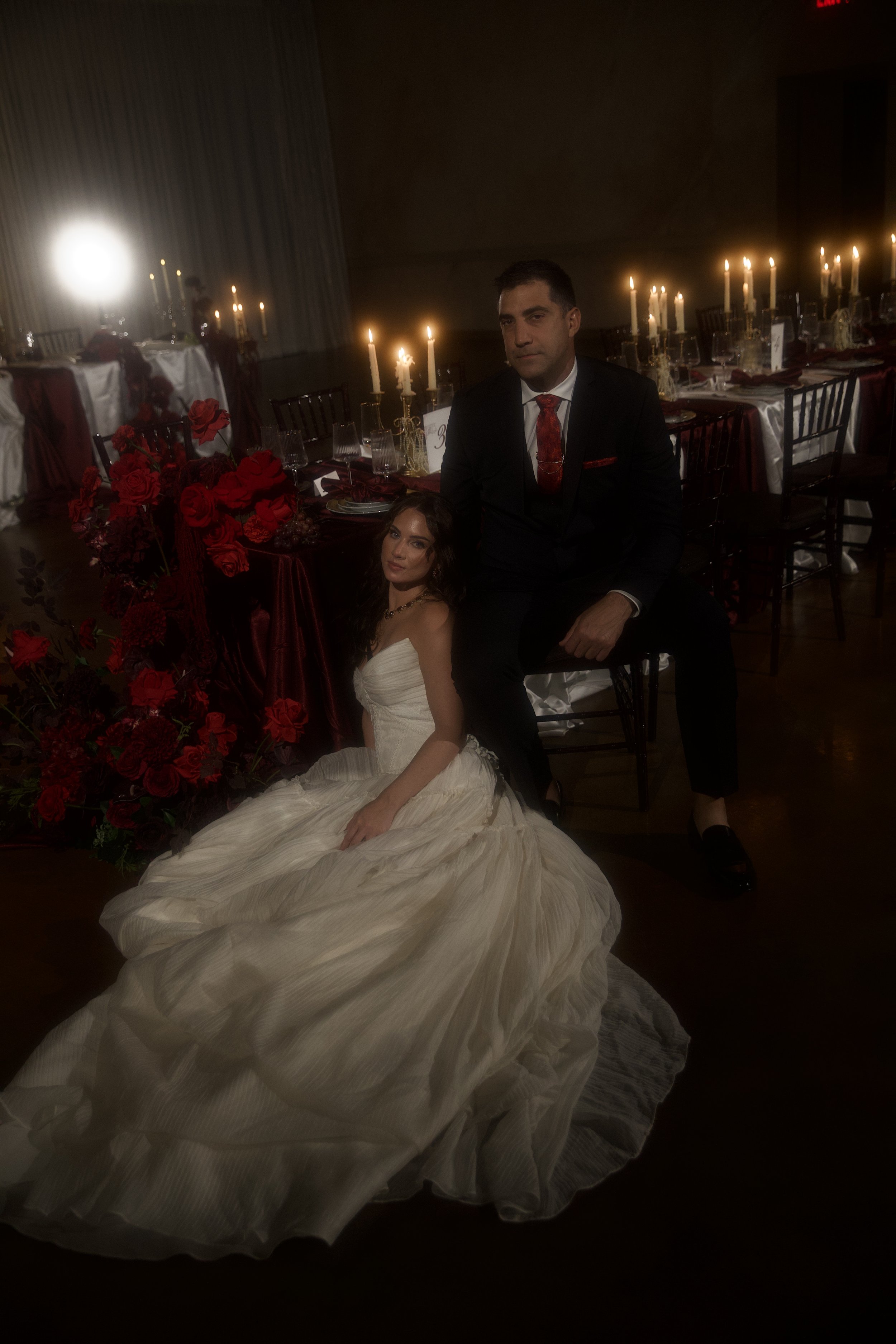 Dark romance wedding inspiration at Bella Sera Event Villa near Pittsburgh, featuring a cascading red and burgundy bridal bouquet and a candlelit staircase filled with dramatic floral arrangements. Floral design by S.R. Event Design & Decor pairs ric