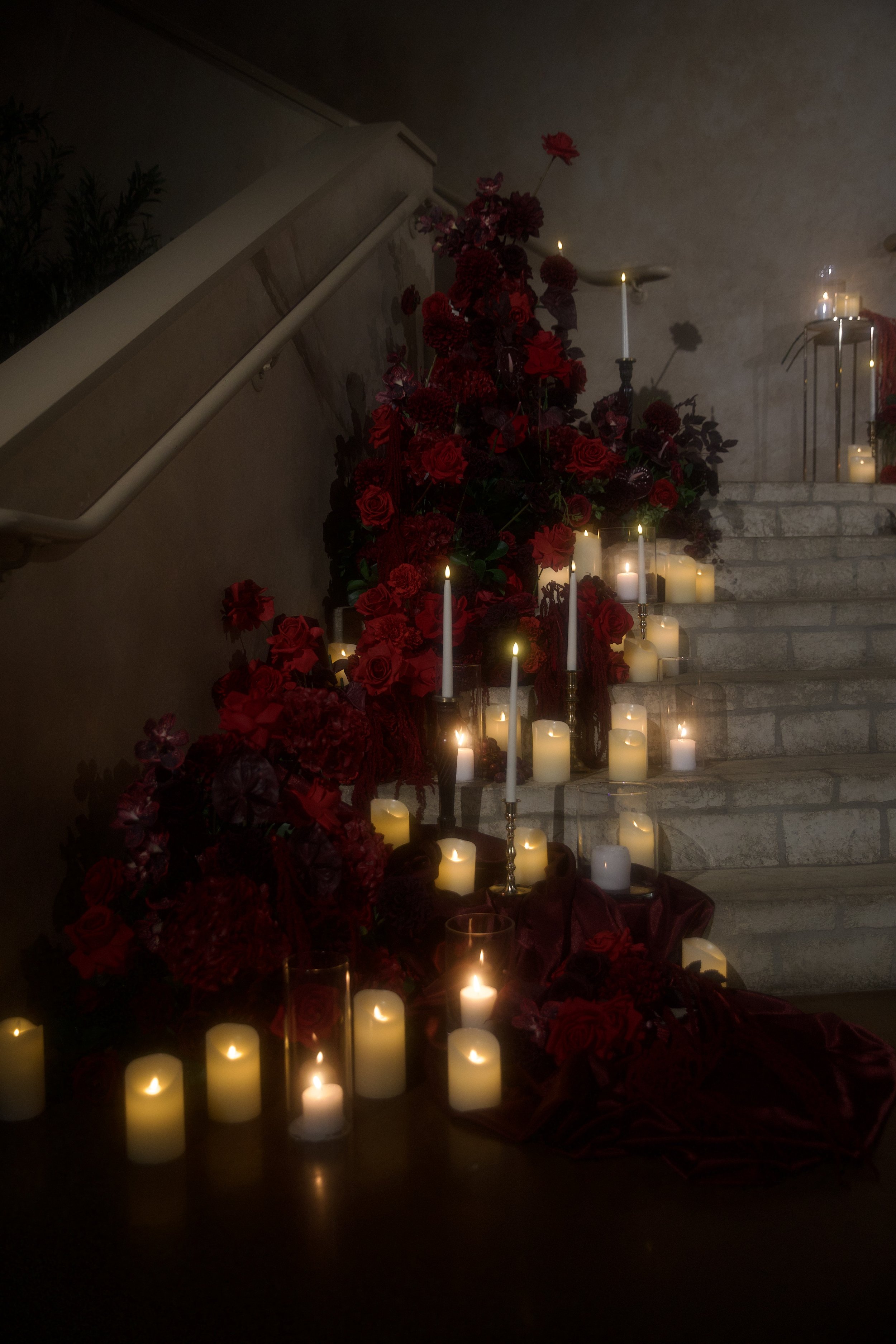 A dramatic wedding staircase floral installation featuring deep red roses, burgundy blooms, cascading amaranthus, and layered candlelight. Designed by S.R. Event Design & Decor for a dark romance styled shoot at Bella Sera Event Villa near Pittsburgh