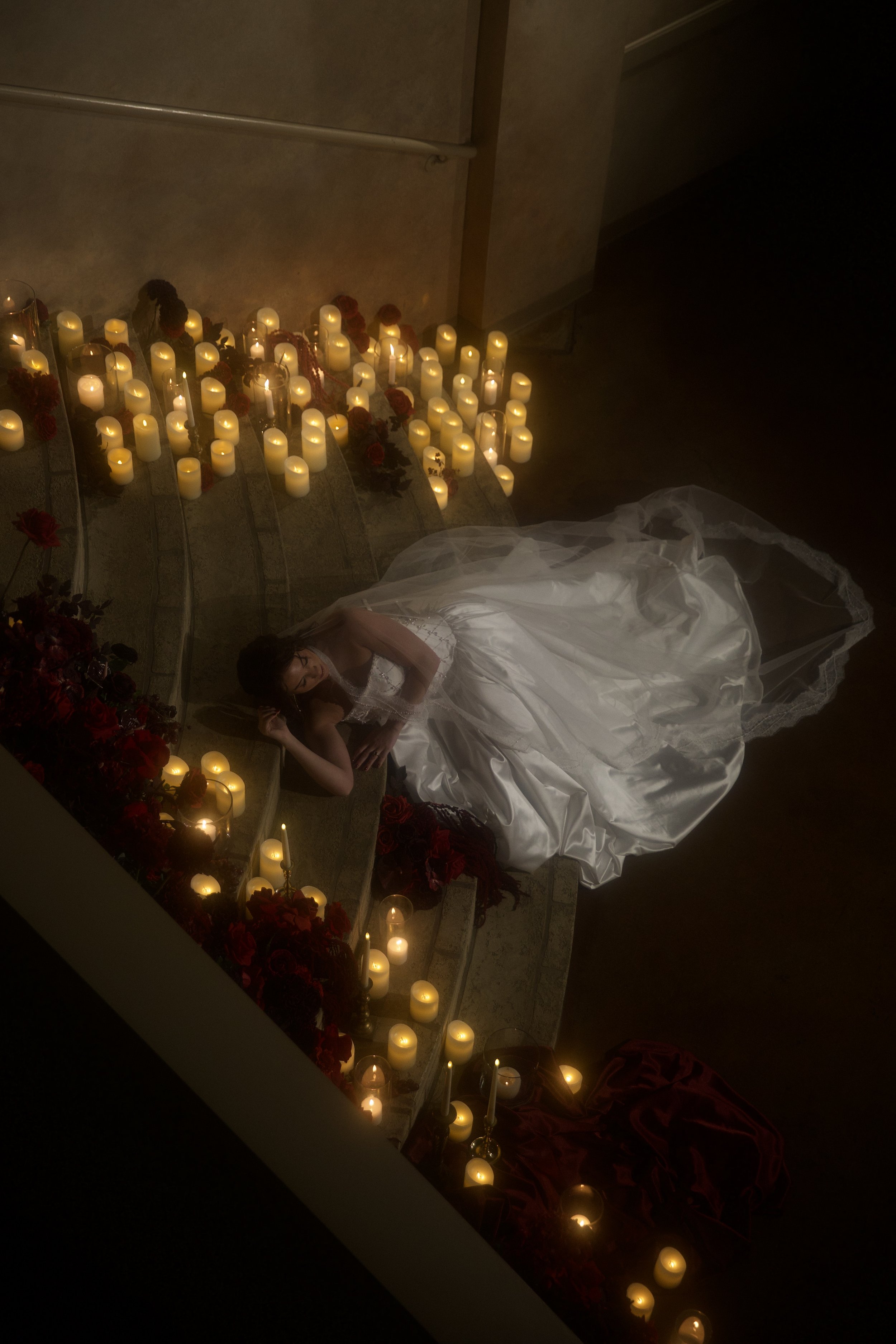 Dark romance wedding inspiration at Bella Sera Event Villa near Pittsburgh, featuring a cascading red and burgundy bridal bouquet and a candlelit staircase filled with dramatic floral arrangements. Floral design by S.R. Event Design & Decor pairs ric