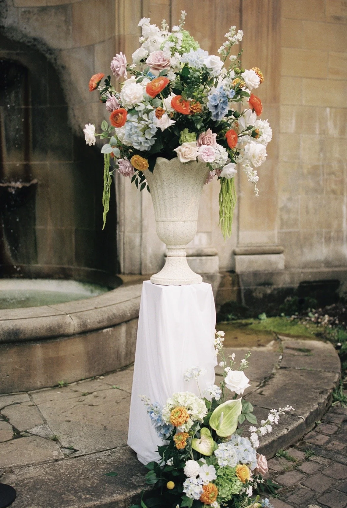 White floral plinths elevated the ceremony urns while complementing the garden’s timeless stone architecture.