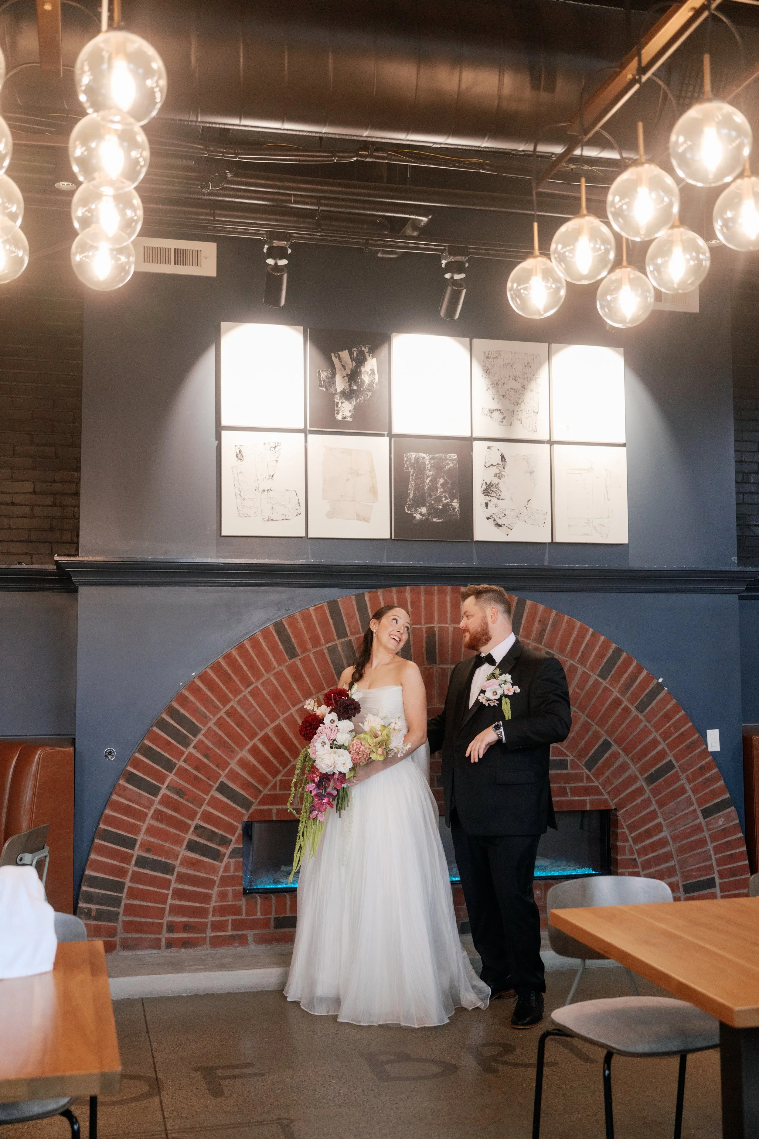 Bride and groom leaning together beside a brick fireplace, with a large blush and burgundy bouquet cascading down the bride’s white gown. @TKPhotoand Film 
Planner : @MadilineKellyevents 
Florist @SREventDesign & Decor 