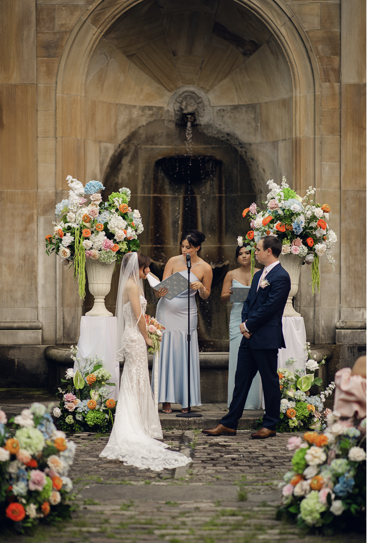 White floral plinths elevated the ceremony urns while complementing the garden’s timeless stone architecture.