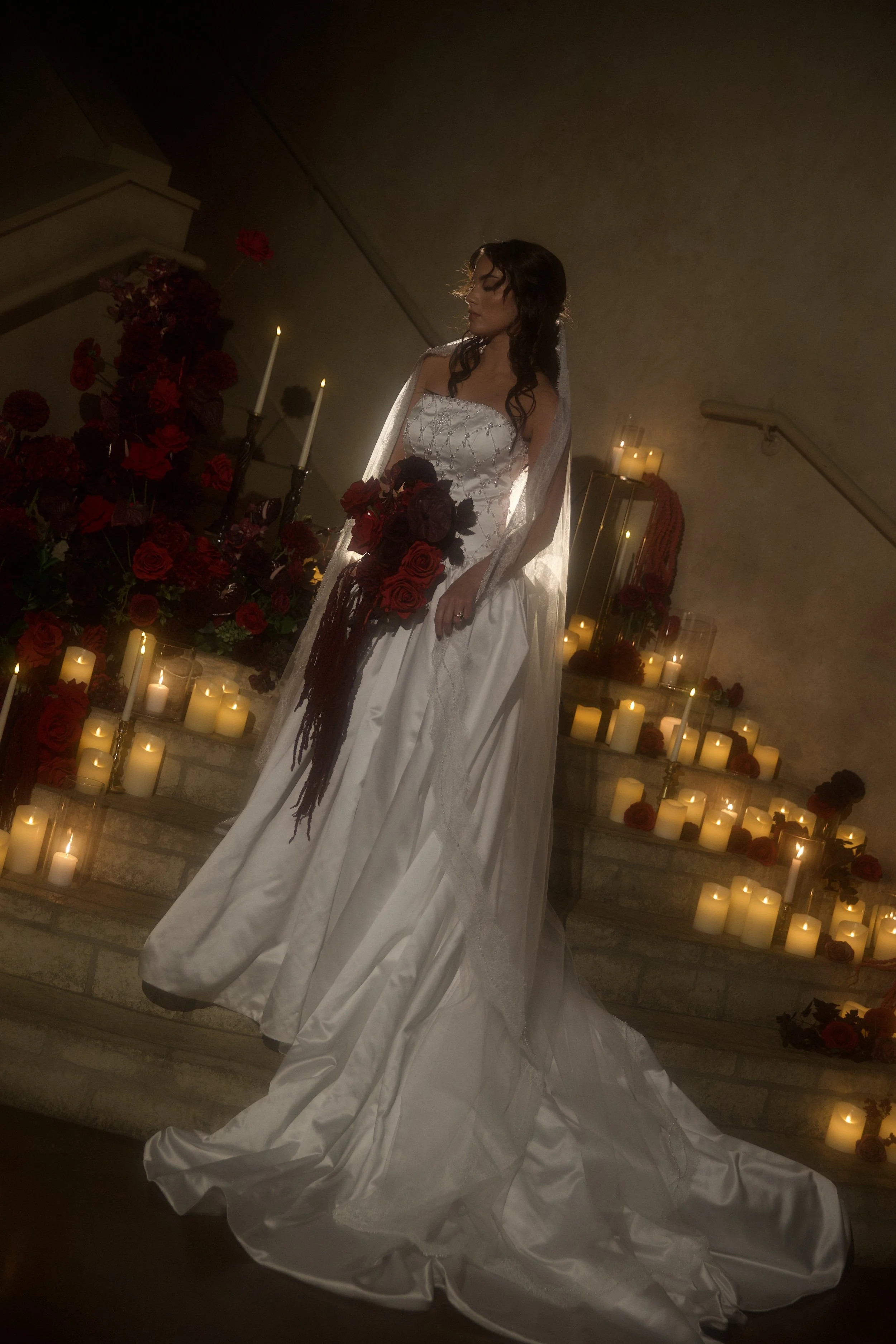 Dark romance wedding inspiration at Bella Sera Event Villa near Pittsburgh, featuring a cascading red and burgundy bridal bouquet and a candlelit staircase filled with dramatic floral arrangements. Floral design by S.R. Event Design & Decor pairs ric