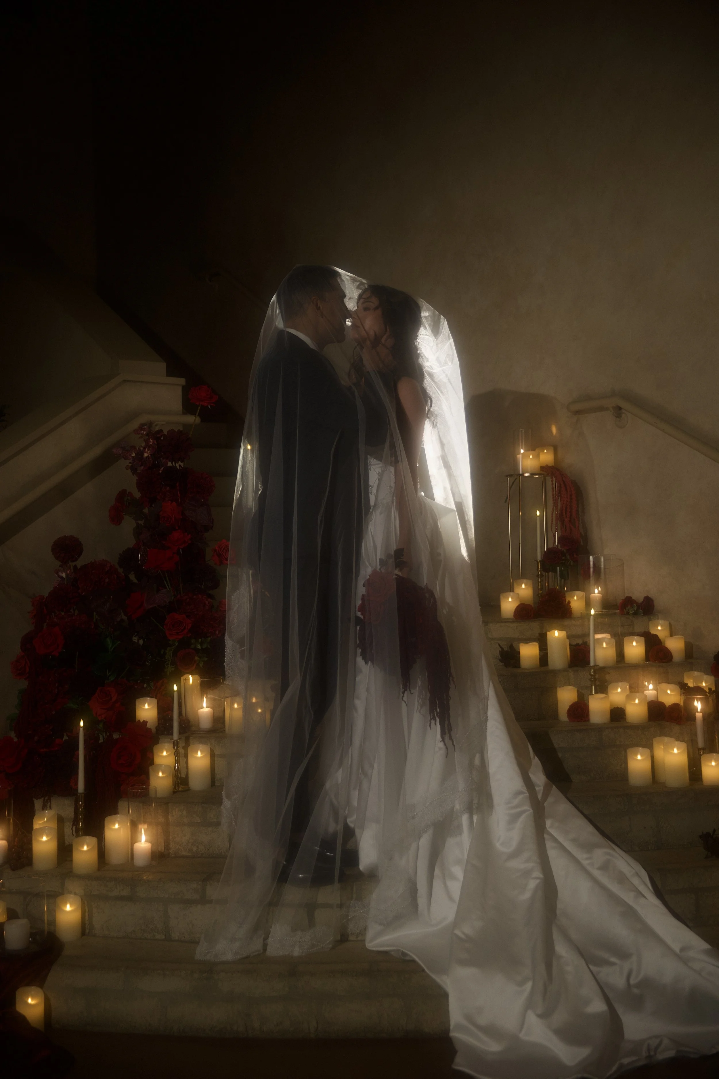 Dark romance wedding inspiration at Bella Sera Event Villa near Pittsburgh, featuring a cascading red and burgundy bridal bouquet and a candlelit staircase filled with dramatic floral arrangements. Floral design by S.R. Event Design & Decor pairs ric