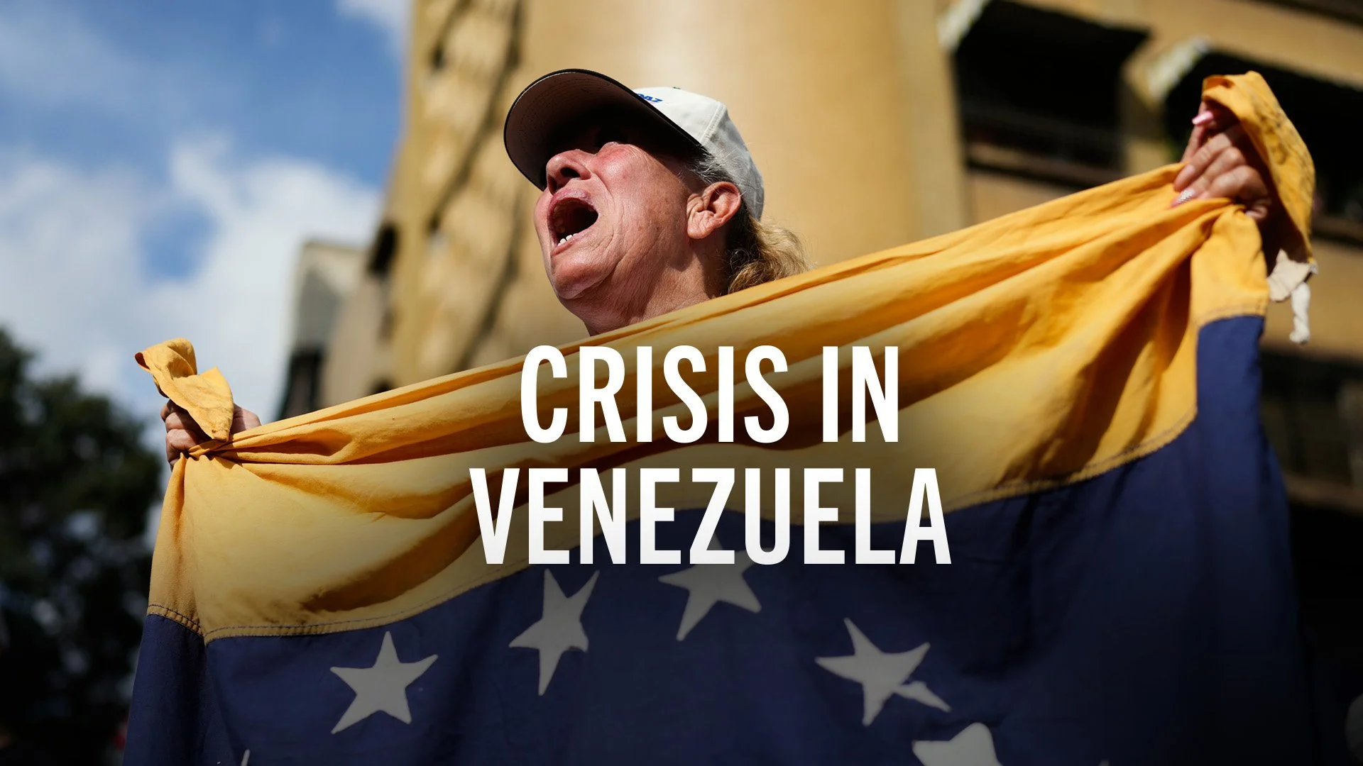 A woman passionately protesting, wearing a baseball cap and holding a yellow flag with a faded blue section and white stars, with the text "Crisis in Venezuela" overlaid.