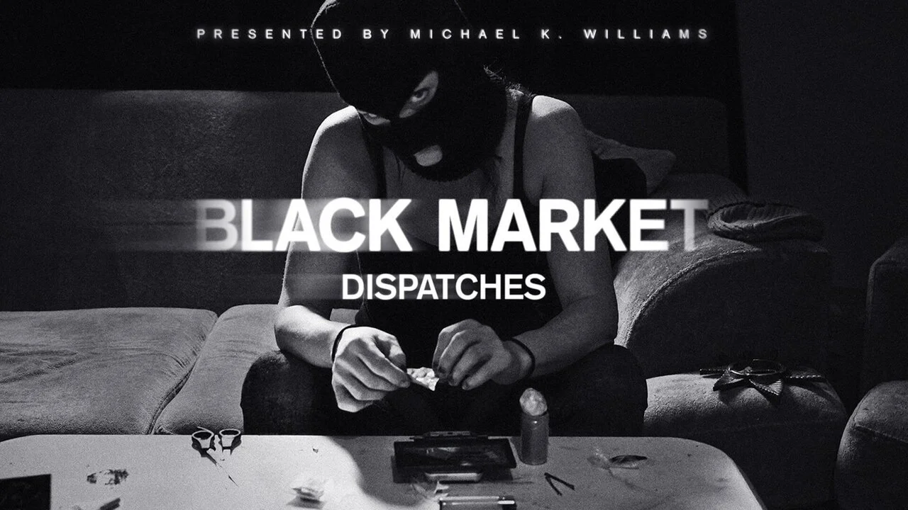 Black and white image of a person wearing a ski mask sitting on a couch, handling small objects on a table, with the text 'Presented by Michael K. Williams' at the top and 'Black Market Dispatches' in the center.