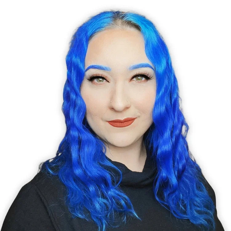 A woman with bright blue wavy hair, light skin, green eyes, and makeup including blue eyebrows and red lipstick, wearing a black top against a white background.