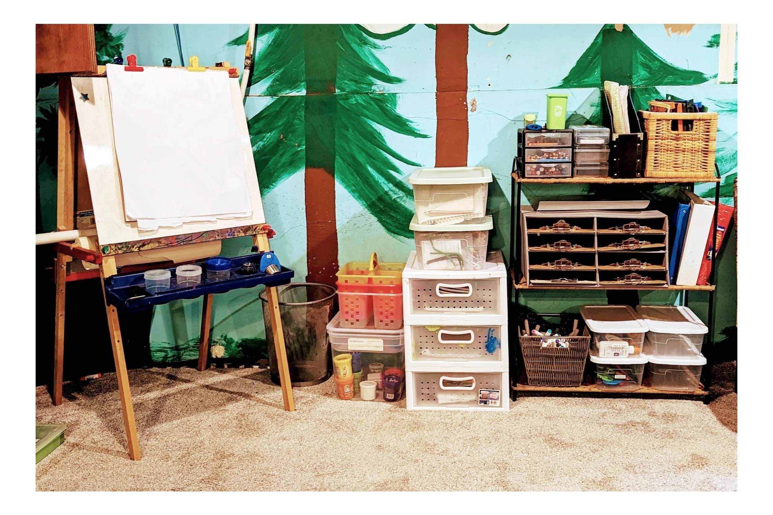 Organized craft supplies and storage containers on shelves and drawers, with a decorated woodland mural background.