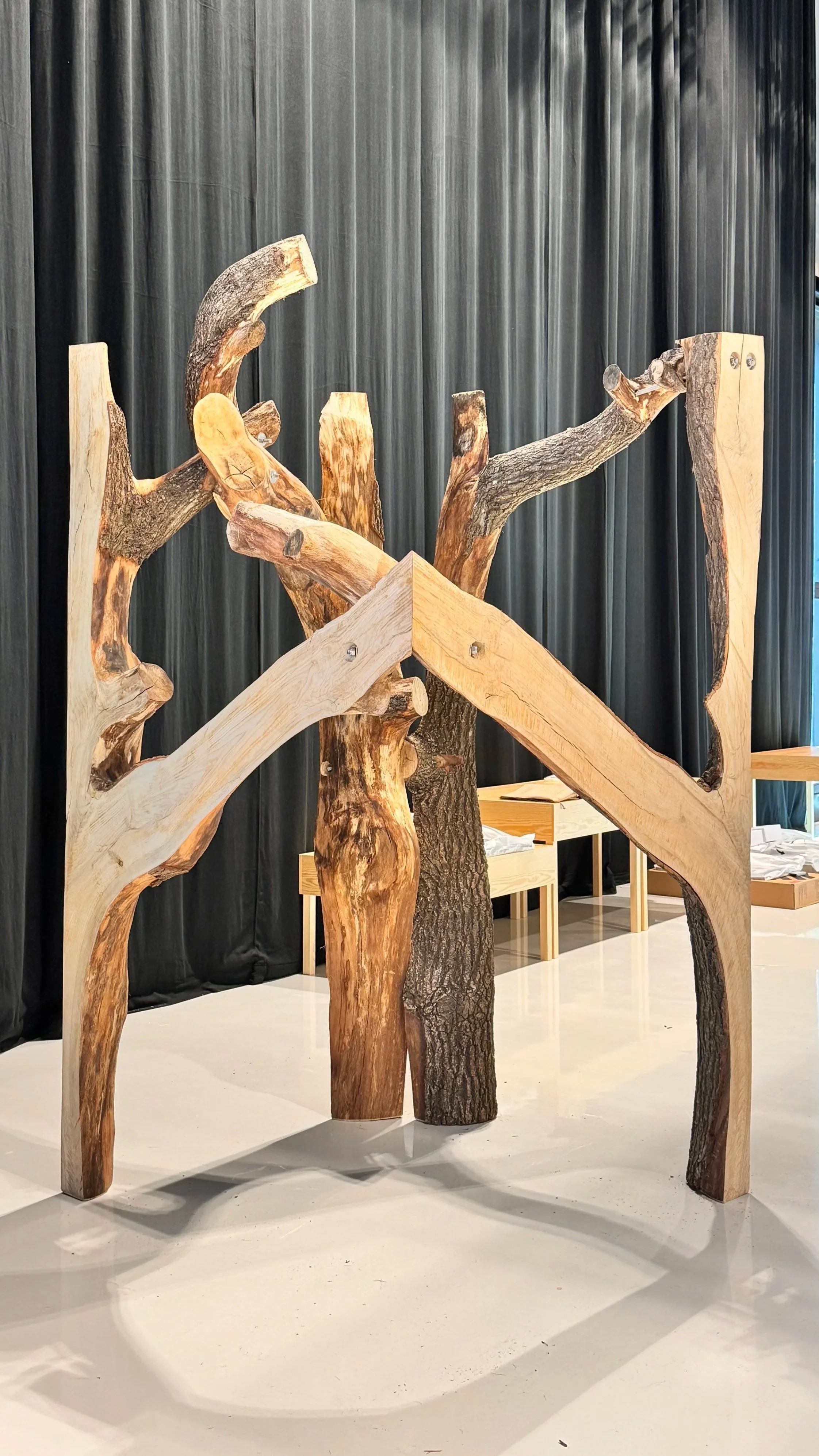 Art installation made of carved and assembled tree branches and trunks, set against a black curtain background.