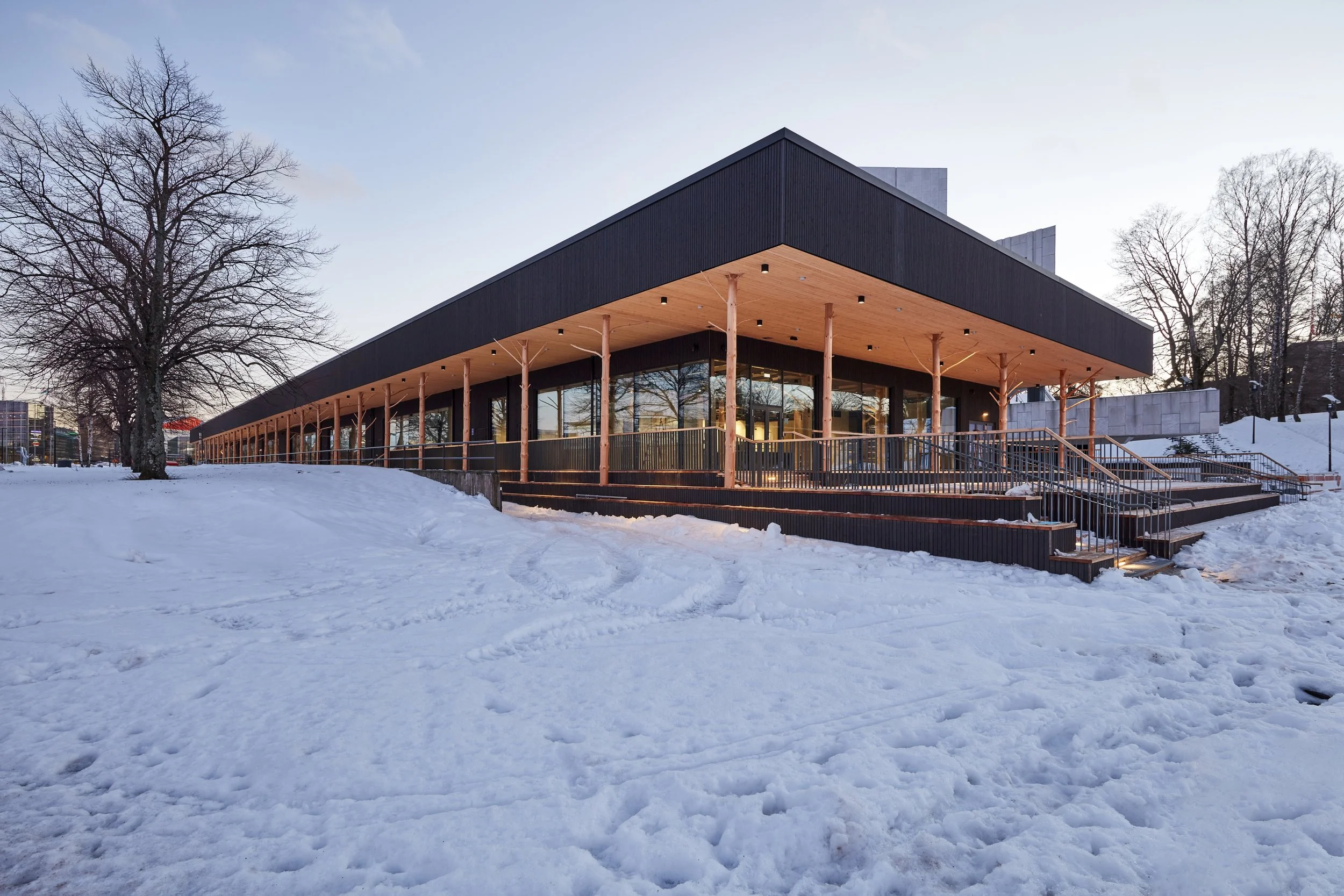 Modern building with large glass windows and a flat roof, supported by wooden columns, in a snowy landscape during winter.