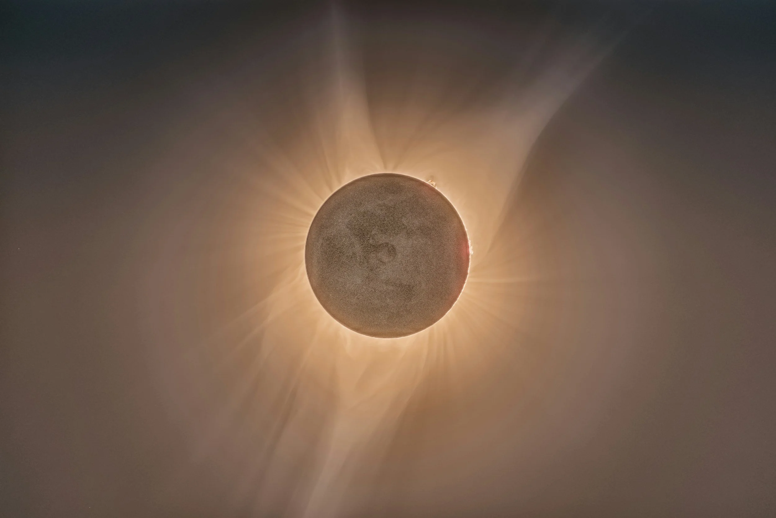 A solar eclipse with the moon covering the sun, creating a bright halo of light with rays radiating outward.
