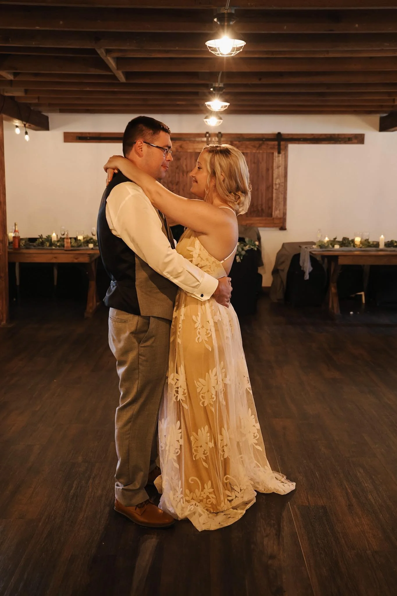A couple dancing in a rustic indoor venue with wooden ceiling beams and soft lighting, celebrating a special occasion.
