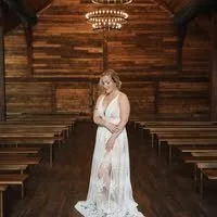 A woman in a white dress standing alone in the center of a rustic wooden chapel.