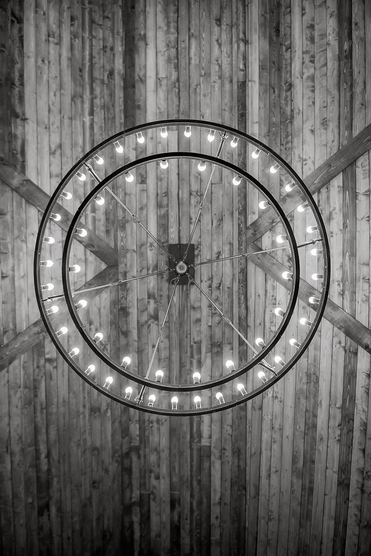 A large, circular chandelier with exposed bulbs hanging from a wooden ceiling.