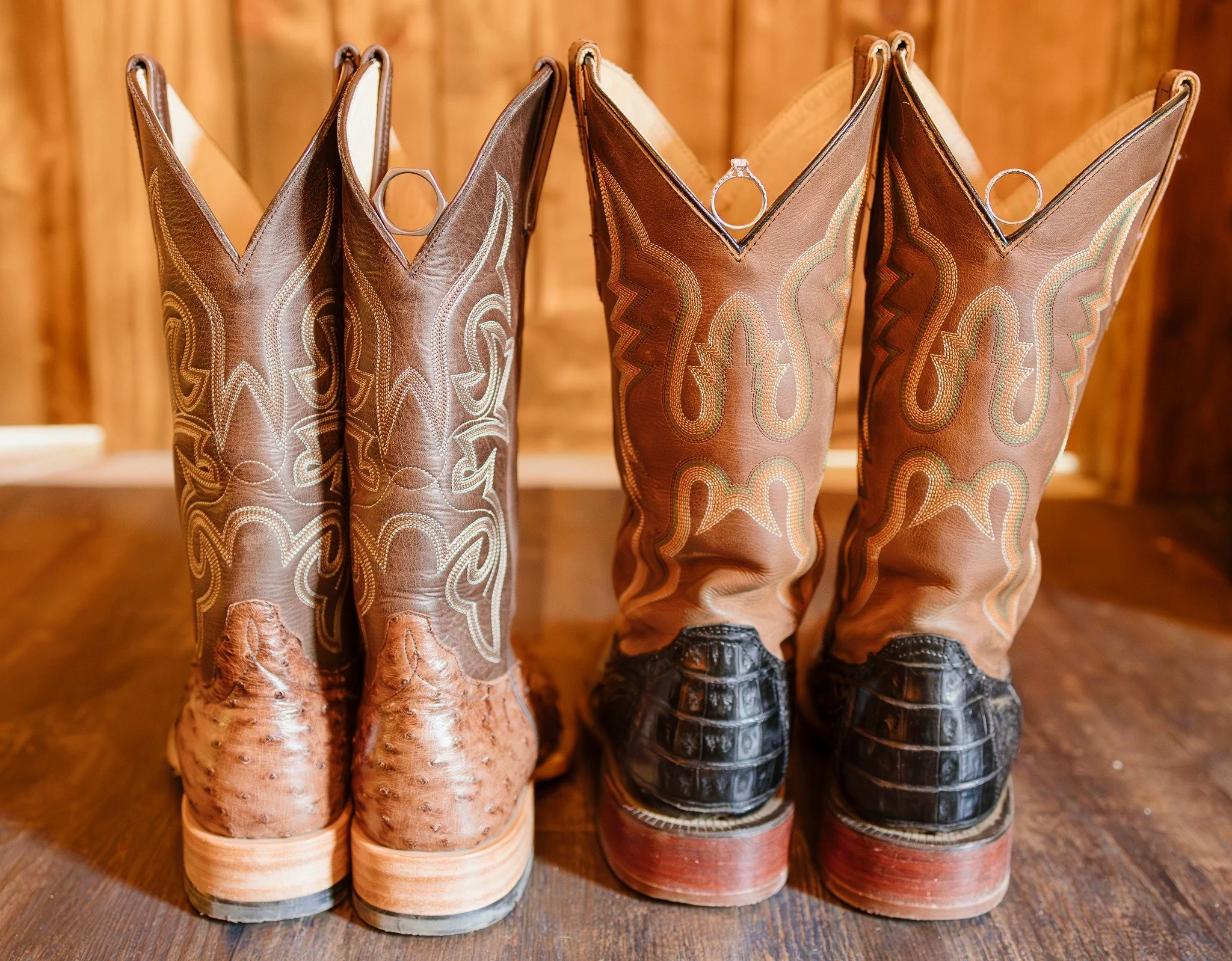 Two pairs of cowboy boots on a wooden surface, one pair with snake skin, the other with crocodile leather, both decorative.