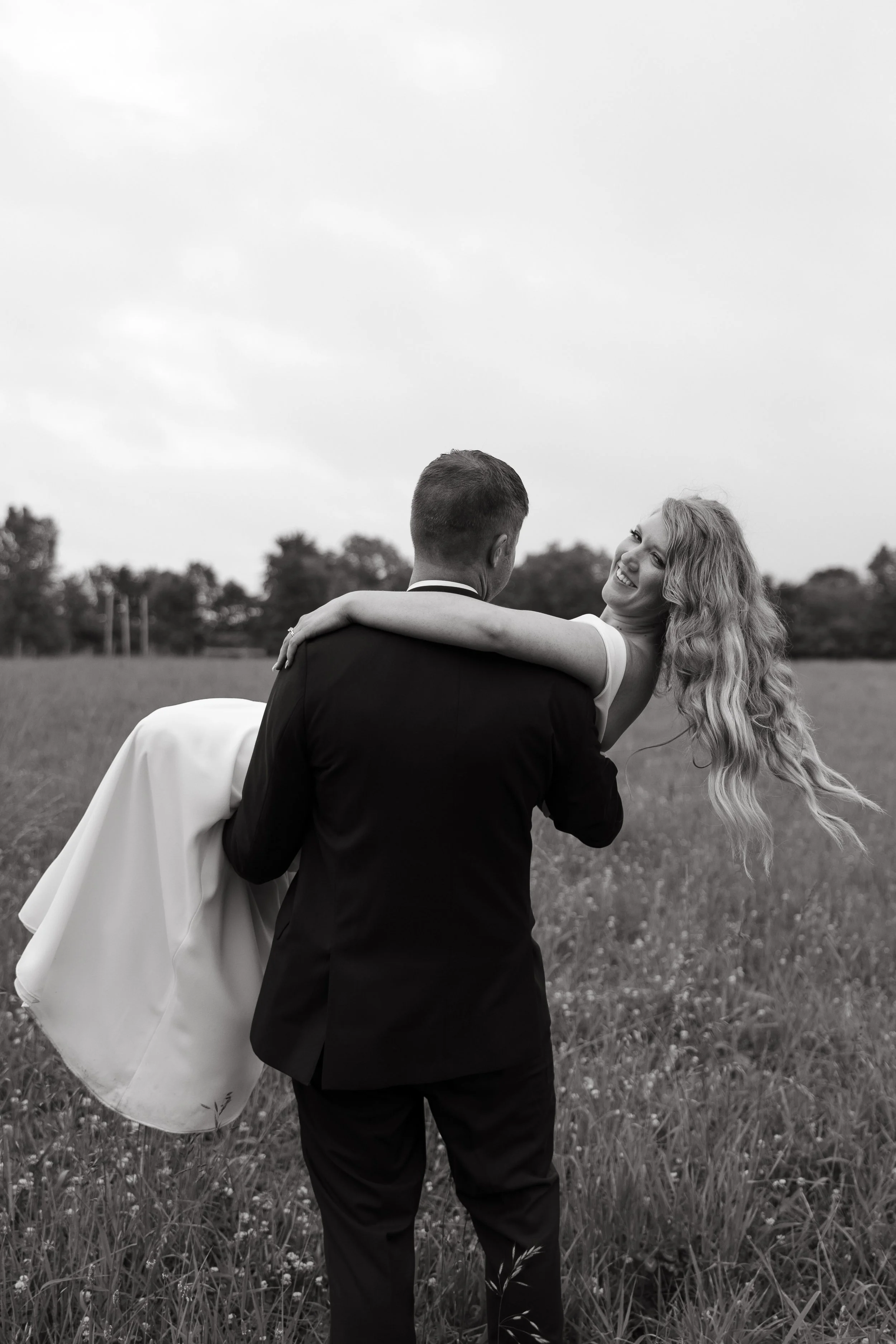 A groom carrying a smiling bride in a field, black and white photo.
