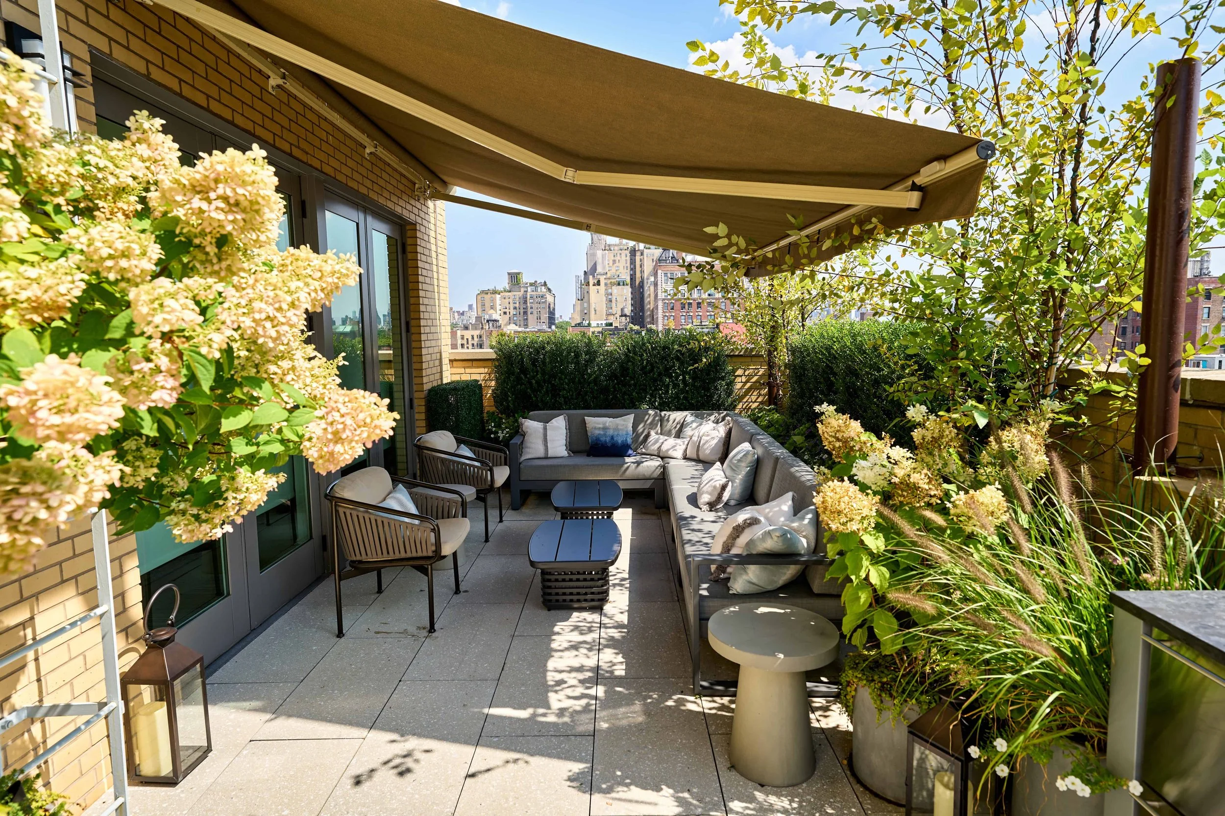 Rooftop garden and NYC penthouse terrace with views of new york city, tall trees, potted plants, flowers, outdoor kitchen and gas grill, landscape lighting and luxury patio furniture