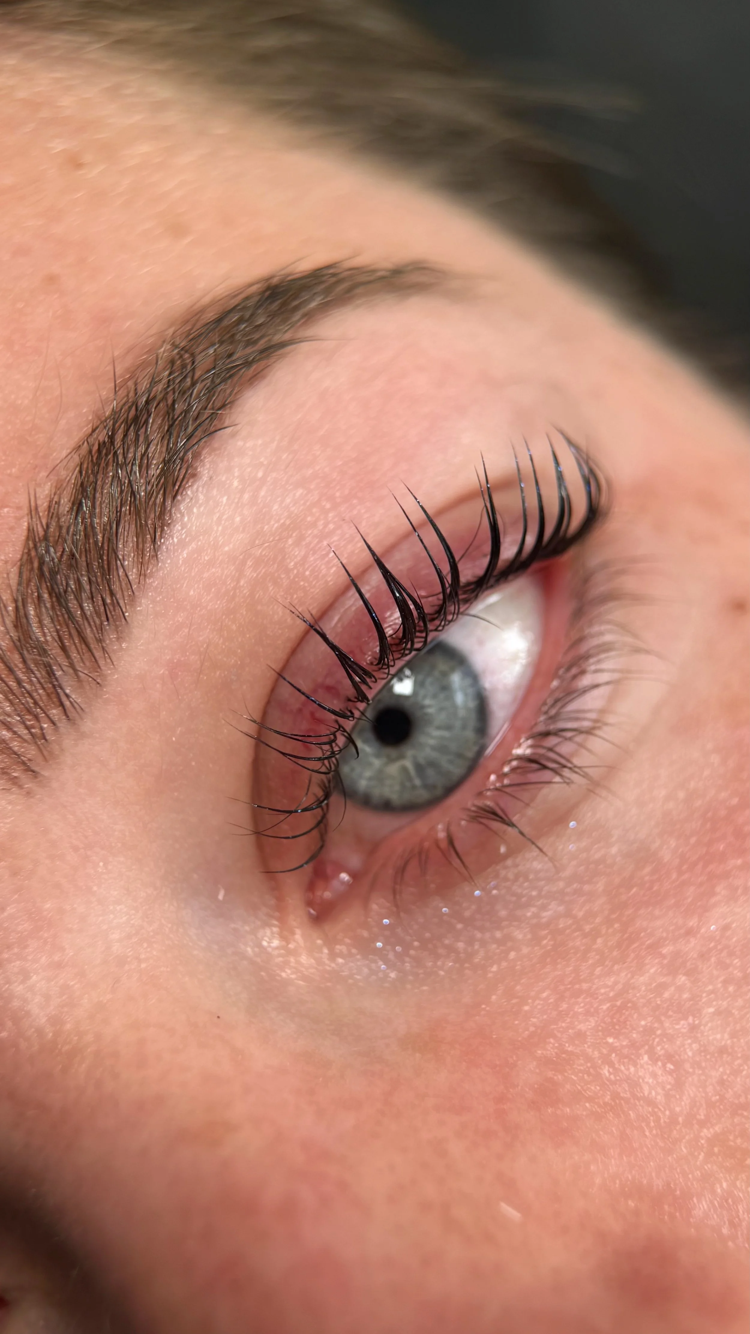 Close-up of a person's eye showing gray iris, long eyelashes, and well-groomed eyebrow.