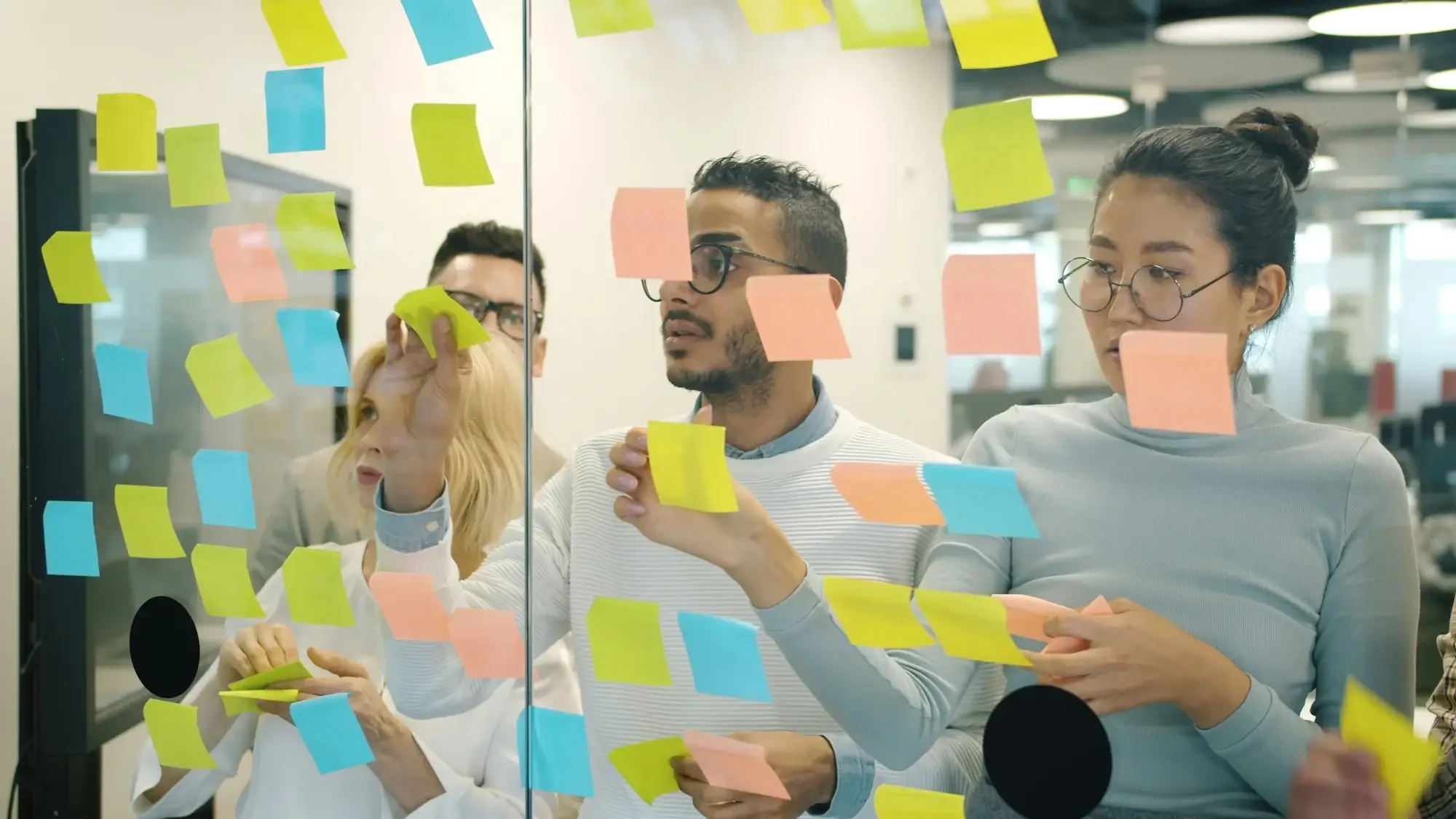 Group of diverse young professionals brainstorming with sticky notes on glass wall in an office.