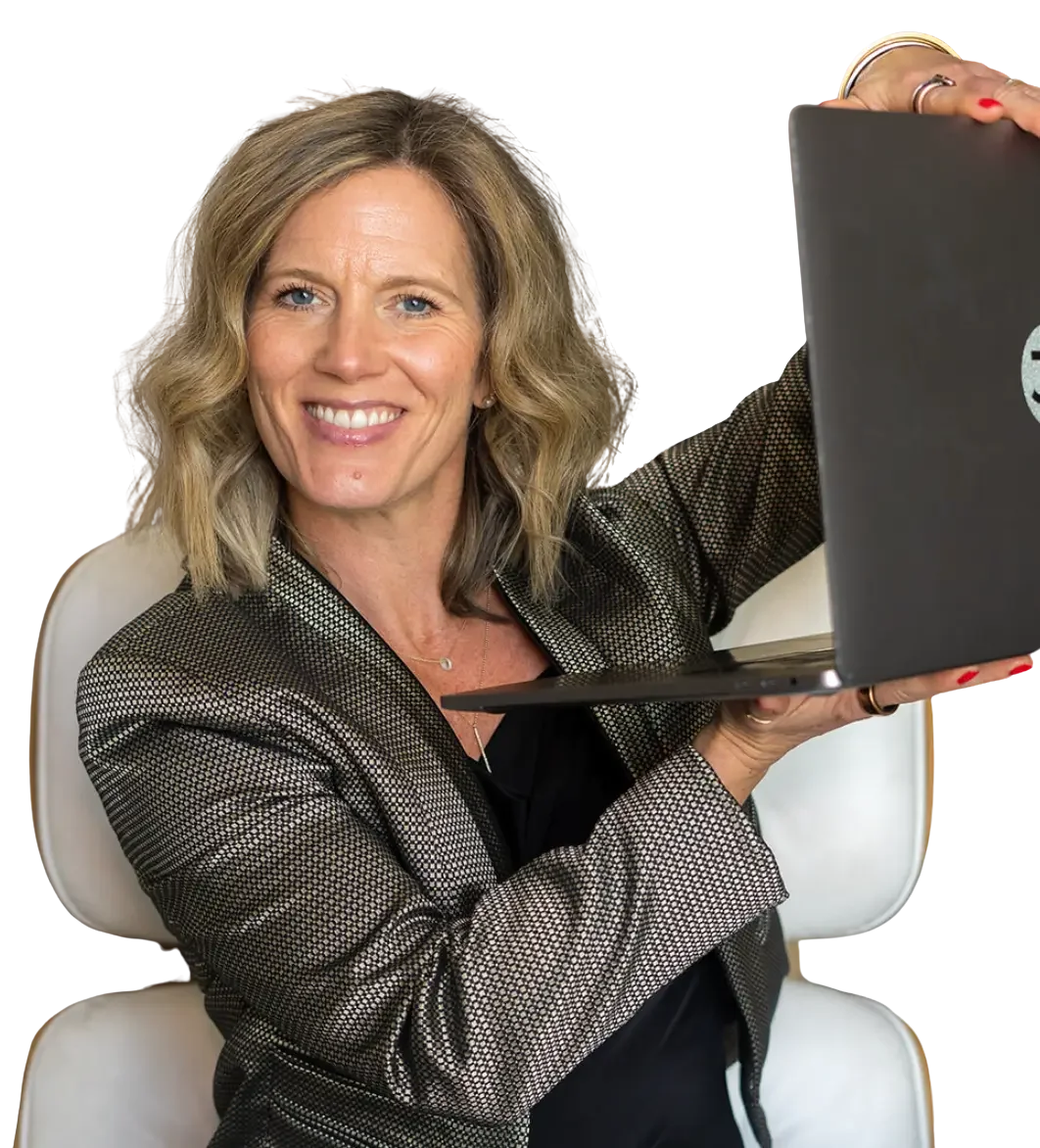 Woman with blonde wavy hair smiling, holding a laptop, sitting on a white chair, dressed in a black and white patterned blazer