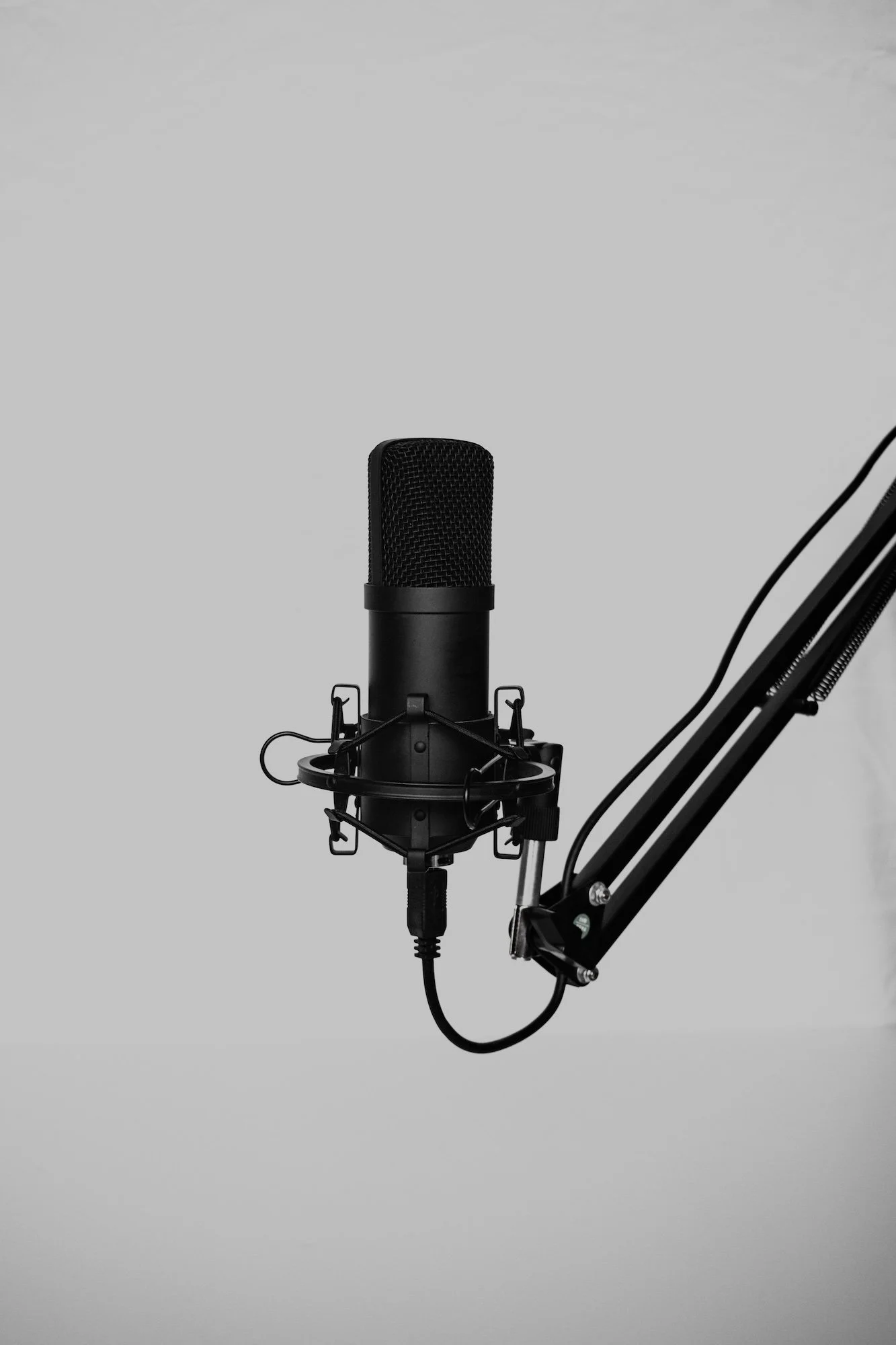 A professional microphone mounted on an adjustable arm against a plain, light gray background.