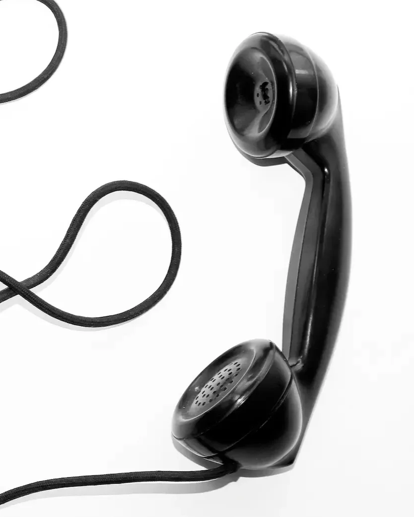 A black wired telephone receiver resting on a white surface with its cord extended.