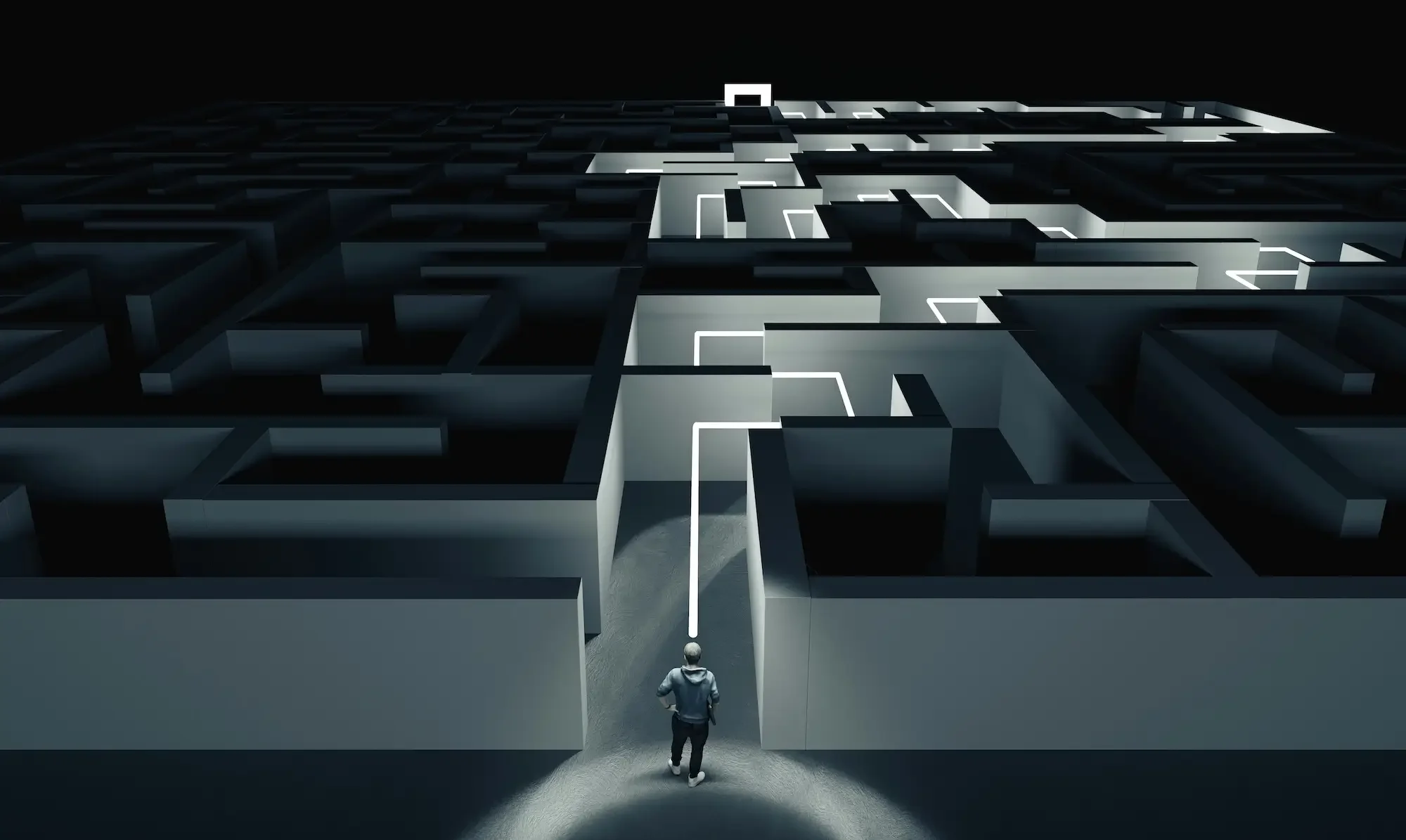 A person walking towards a large illuminated maze at night with high walls and dark surroundings.