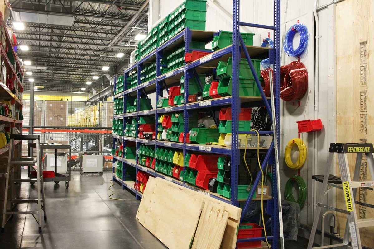 Interior of a warehouse with shelves of colored bins containing small hardware parts, and coiled hoses on the wall.