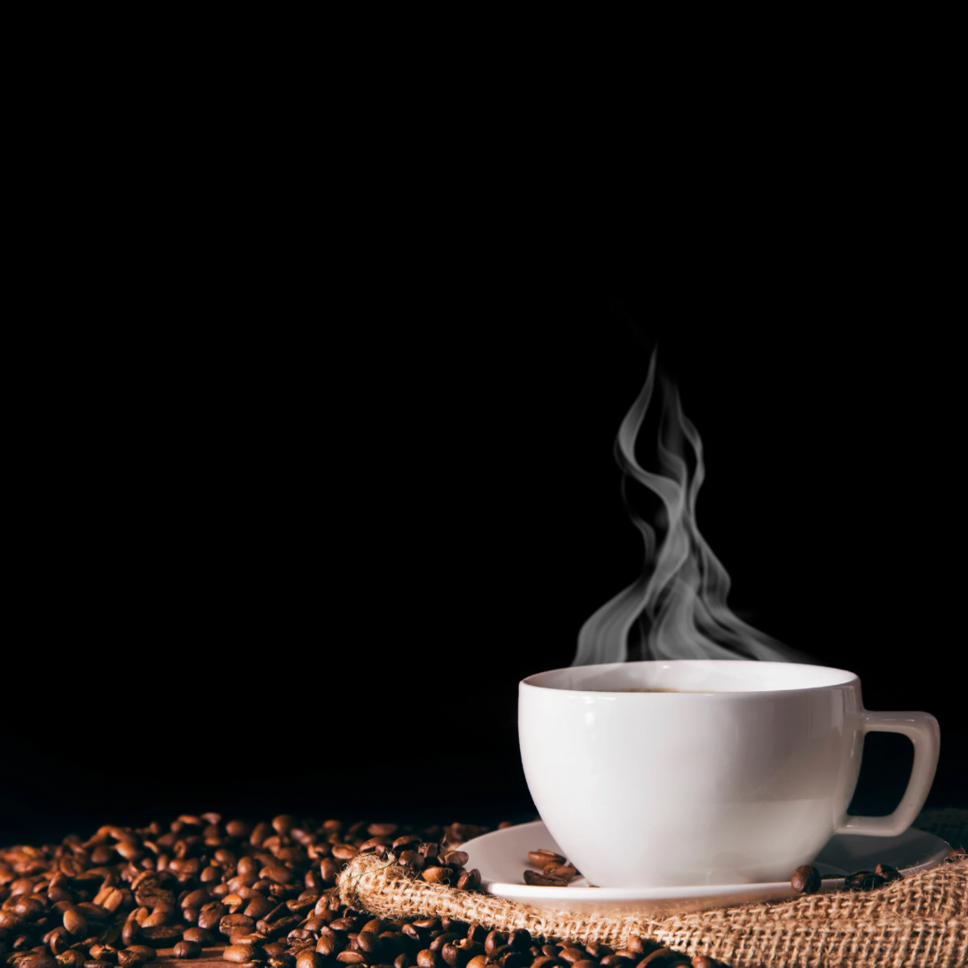 Een witte kop koffie met damp die opstijgt, omringd door koffiebonen op een rijstepad en een stuk jute stof, tegen een zwarte achtergrond.