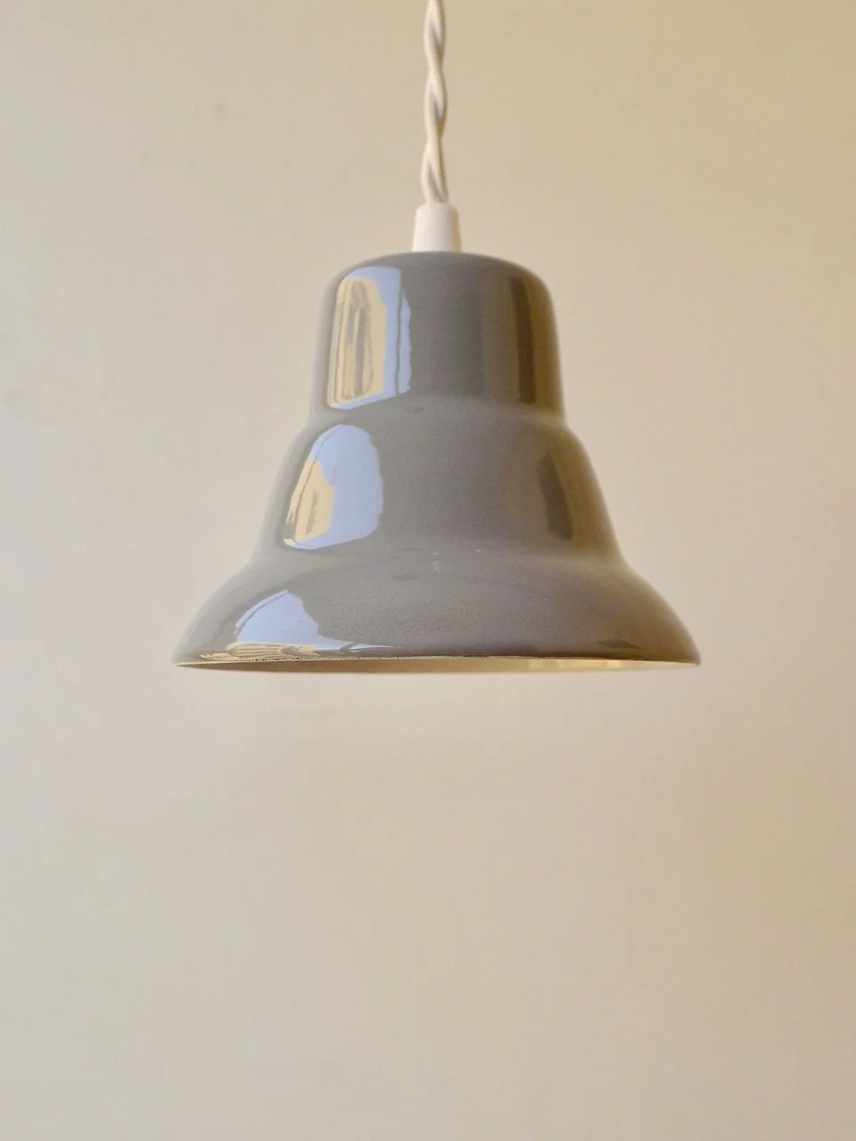 Gray pendant light with a bell-shaped shade. The light fixture is suspended from a white cord and ceiling mount. The shade has a glossy finish and reflects the surrounding environment.