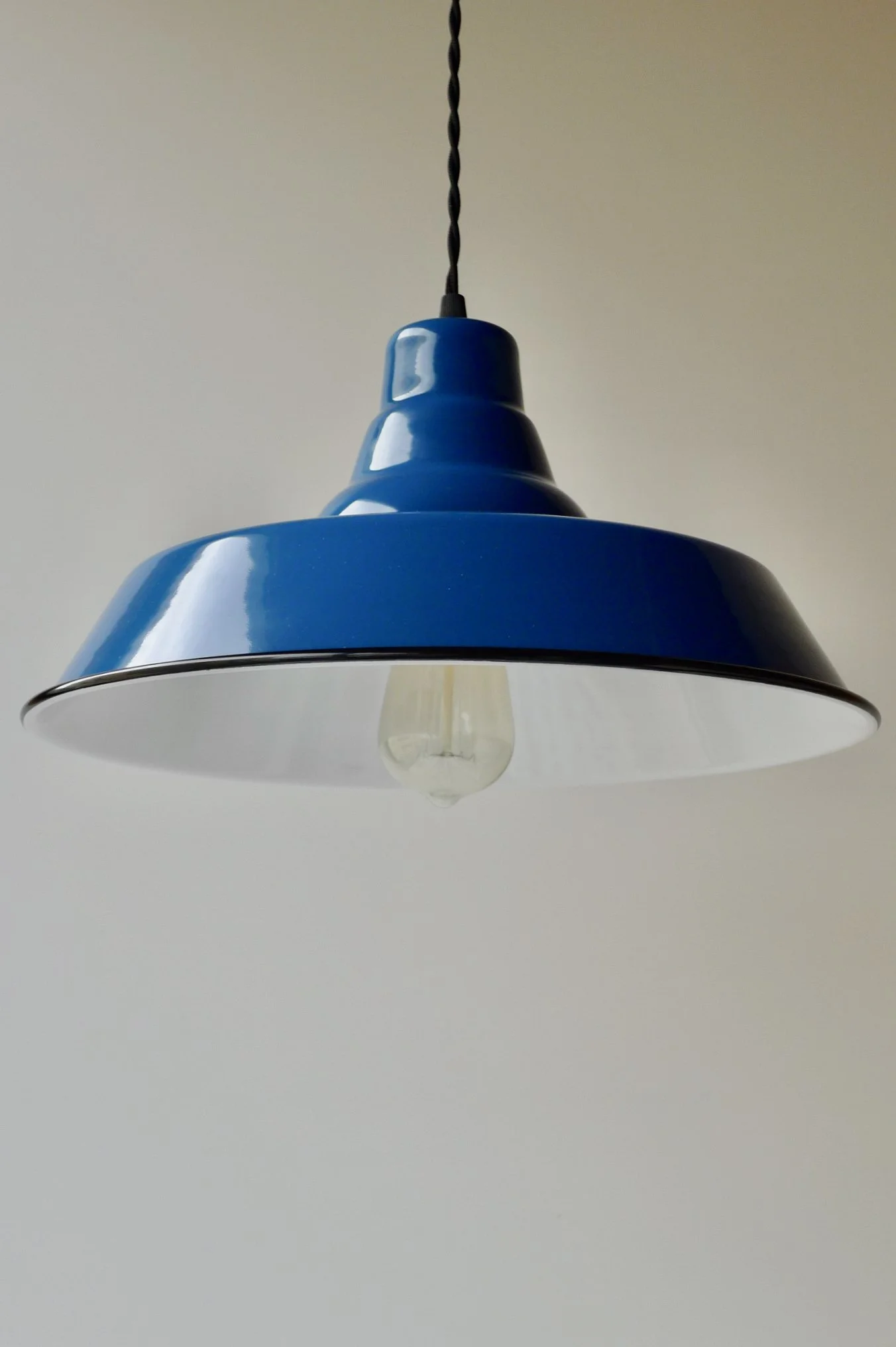 Blue pendant light fixture with a visible bulb, hanging from a black twisted cord against a plain light-colored ceiling.
