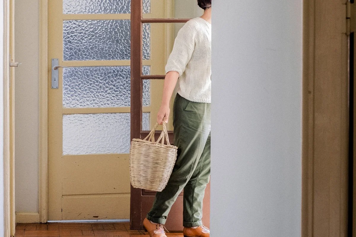 Person holding a wicker basket standing near a door with glass panels in a cozy home interior.