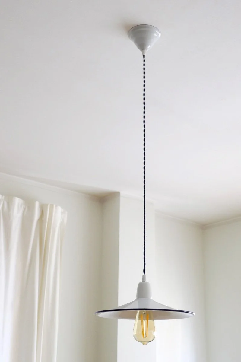 White pendant light fixture with an exposed Edison-style light bulb hanging from a dark-blue twisted cord in a bright room with white walls and a cream curtain.