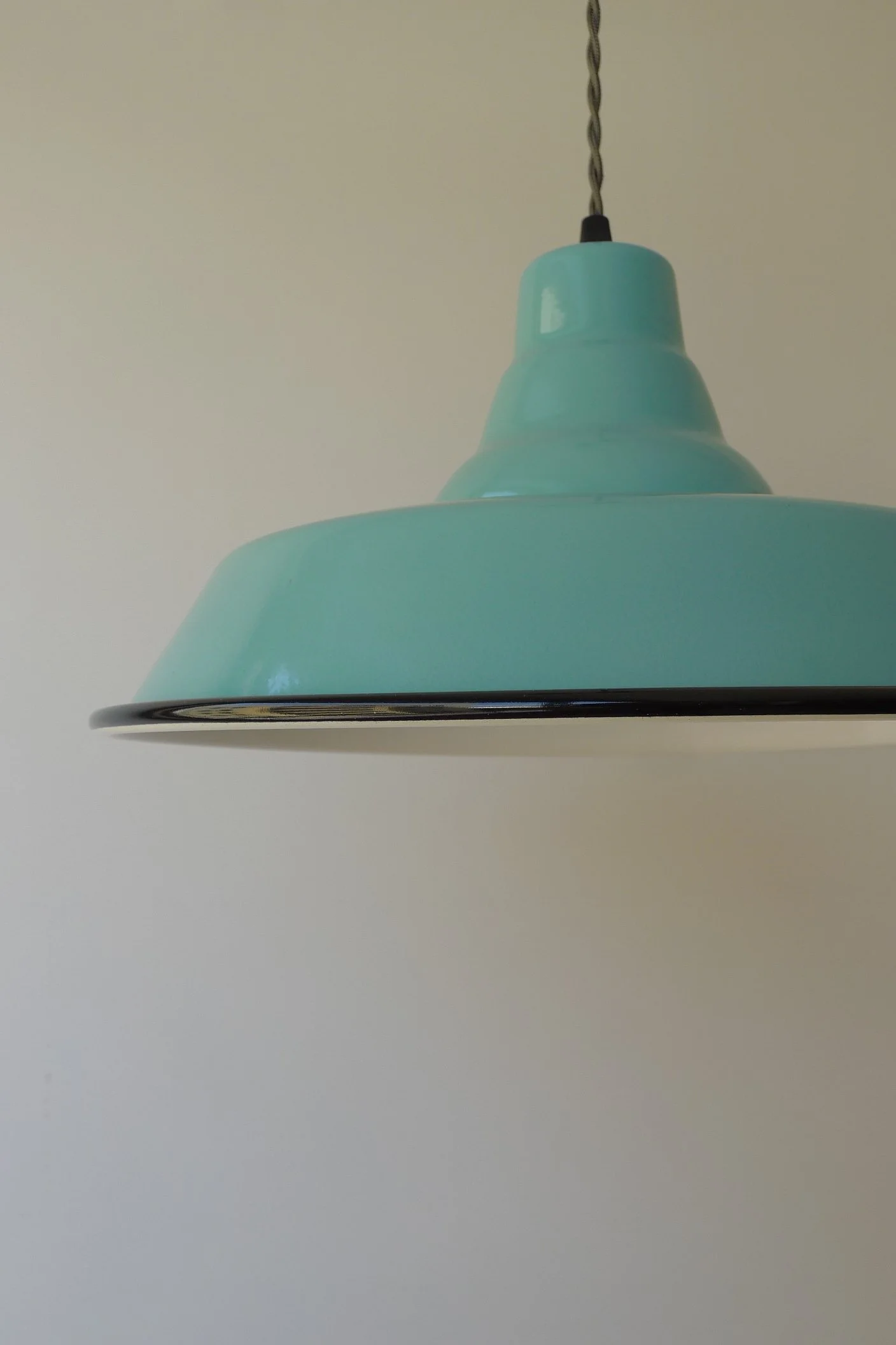 Close-up of a light green hanging pendant lamp against a plain wall.