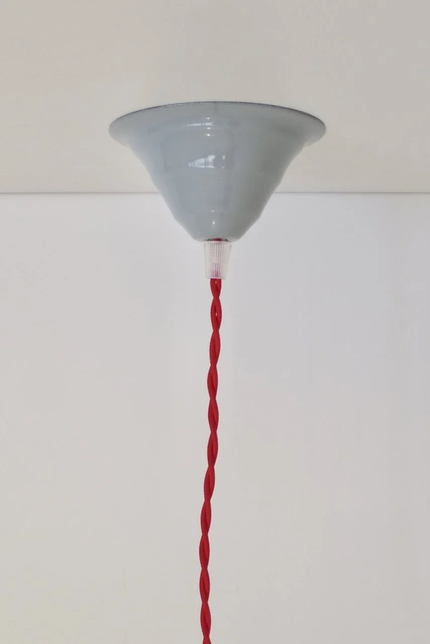 A ceiling-mounted enamel ceiling rose with a red cord hanging downward.