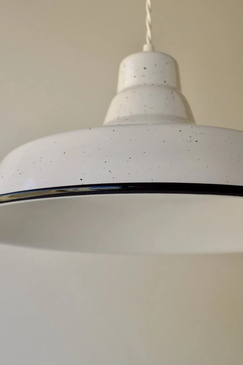 Close-up of a white hanging pendant light with black speckles, photographed from below against a neutral wall.