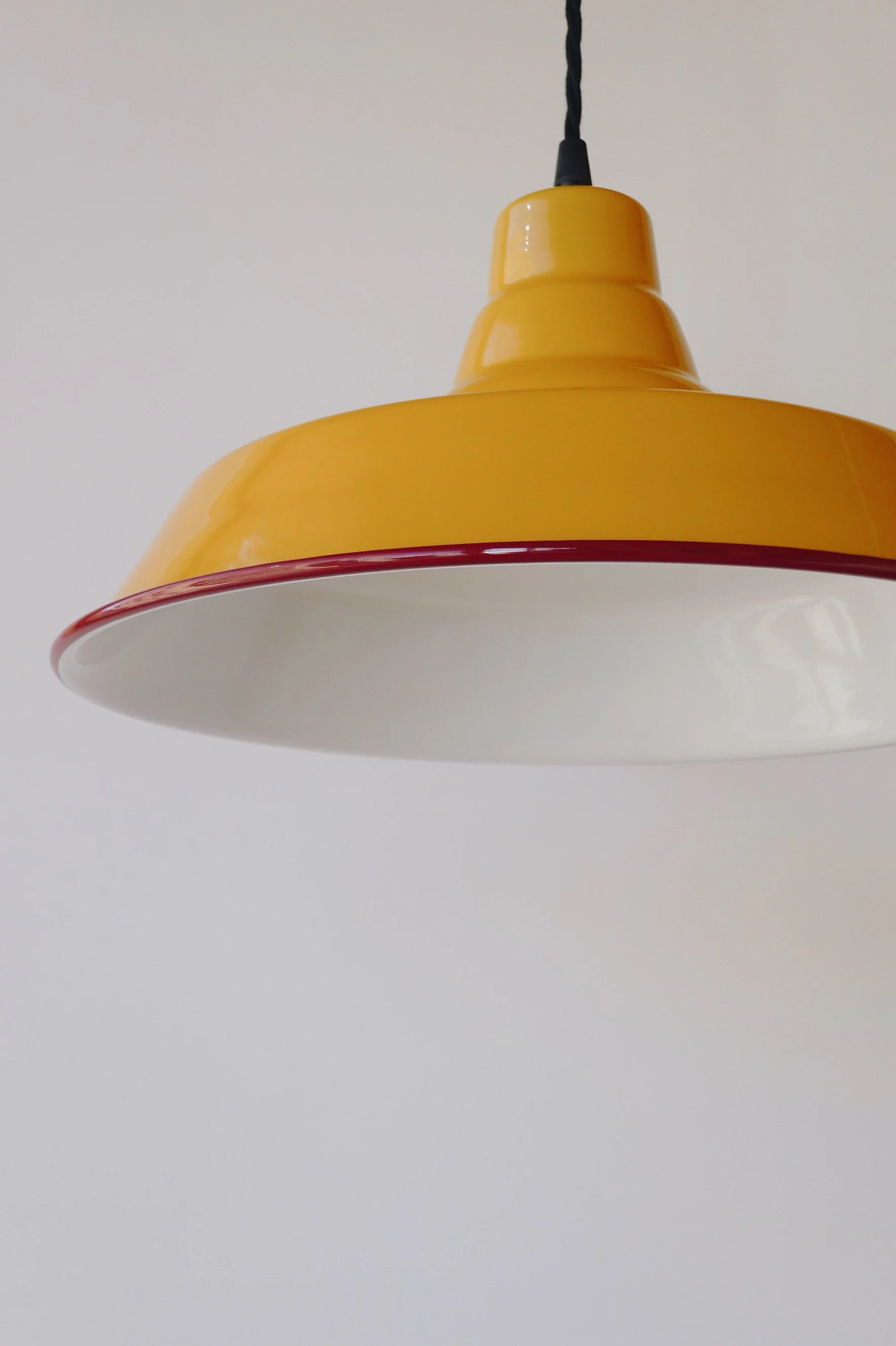 Close-up view of an ochre yellow pendant light fixture hanging from a black cord against a plain white wall.